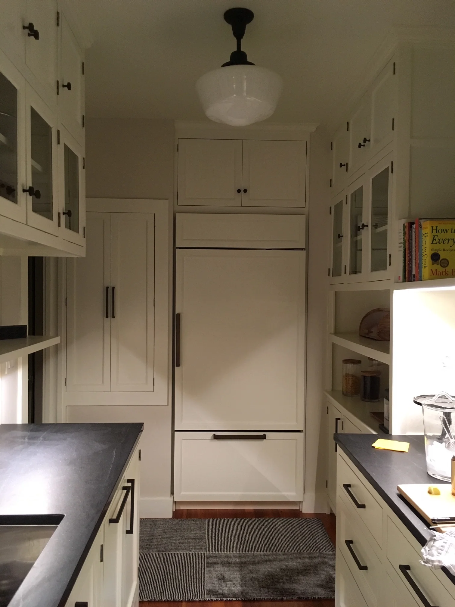  sides of the galley kitchen, glass upper cabinets to match the existing, intermediate floating shelves, counters, tile backsplash, built-in panel front appliances, a range and hood, hardwood floors, and lighting. 