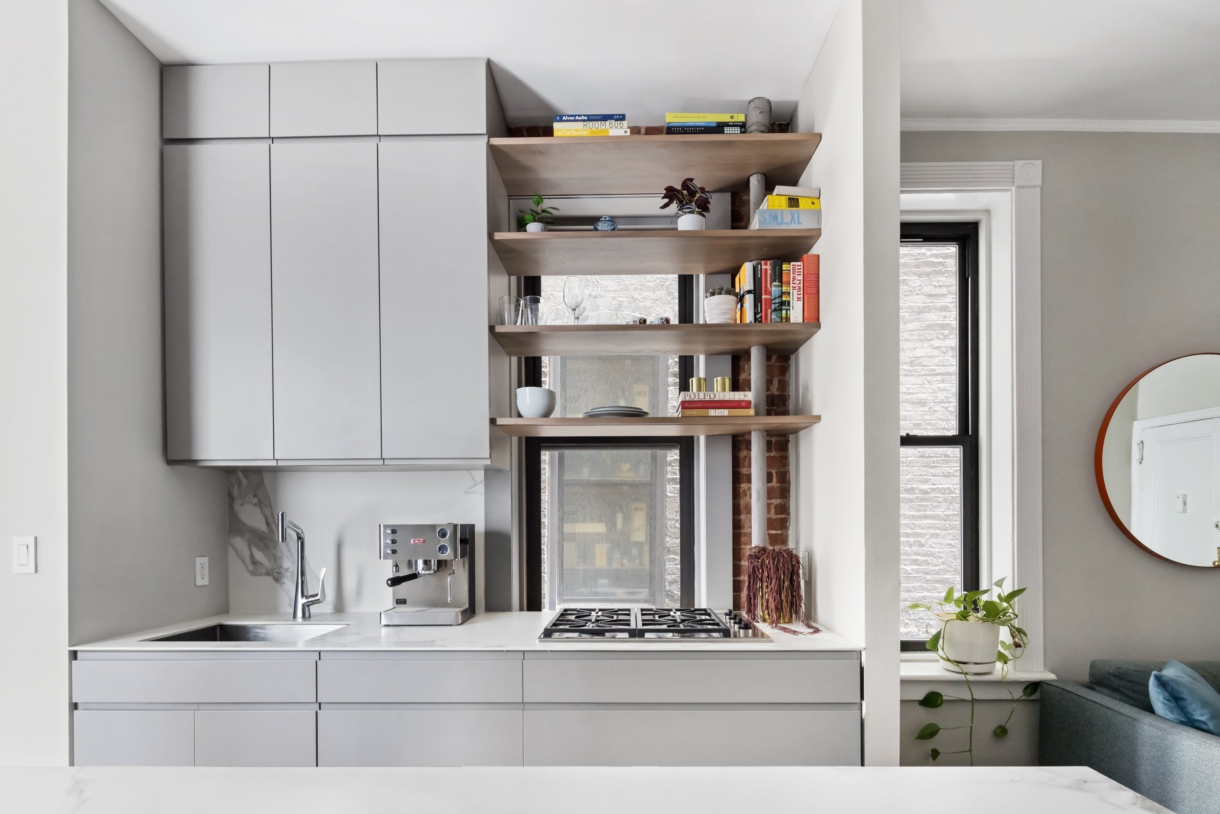cooktop, and downdraft ventilation hood as well as deep drawers, upper cabinets, and open shelves at the window. We then created a large, expansive island housing a hidden, custom-designed pull-out dropleaf dining table at the west end and undercoun