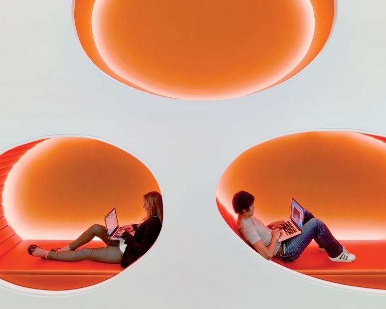 Employees recline in the vinyl-upholstered seating pods of a vertical break-out area.