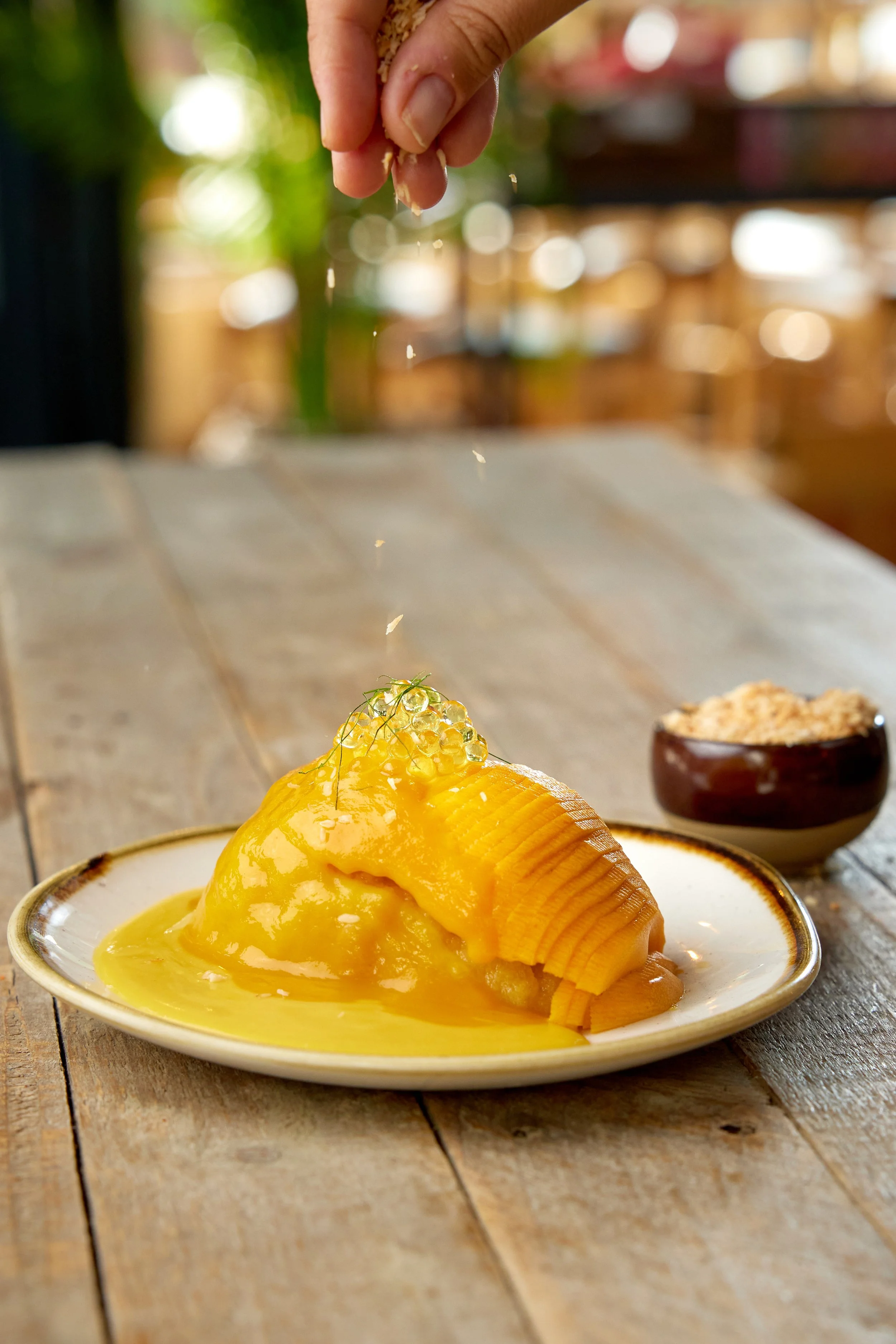 Thai mango sticky rice with coconut mango cream sauce, toasted coconut and mango pearls on a plate