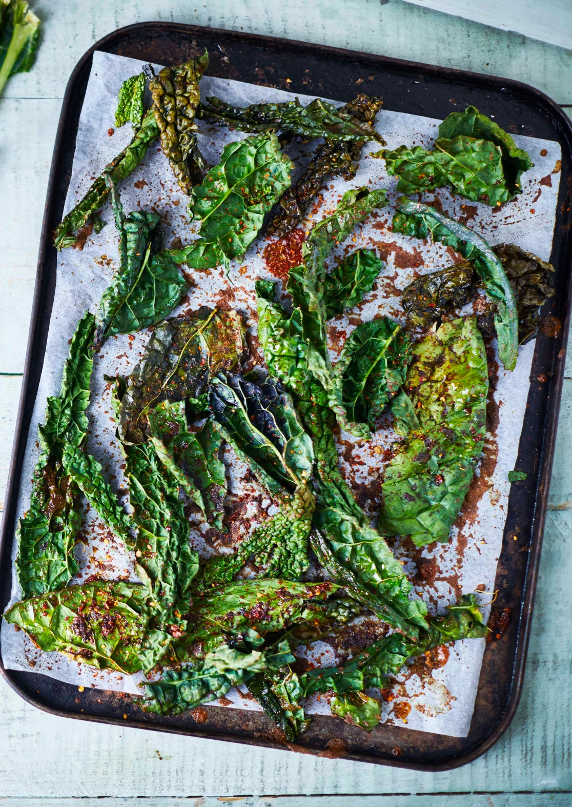 Crispy chilli and Szechuan peppercorn cavolo nero leaves on a dark baking tray with sweet soy glaze, recipe by Sebby Holmes