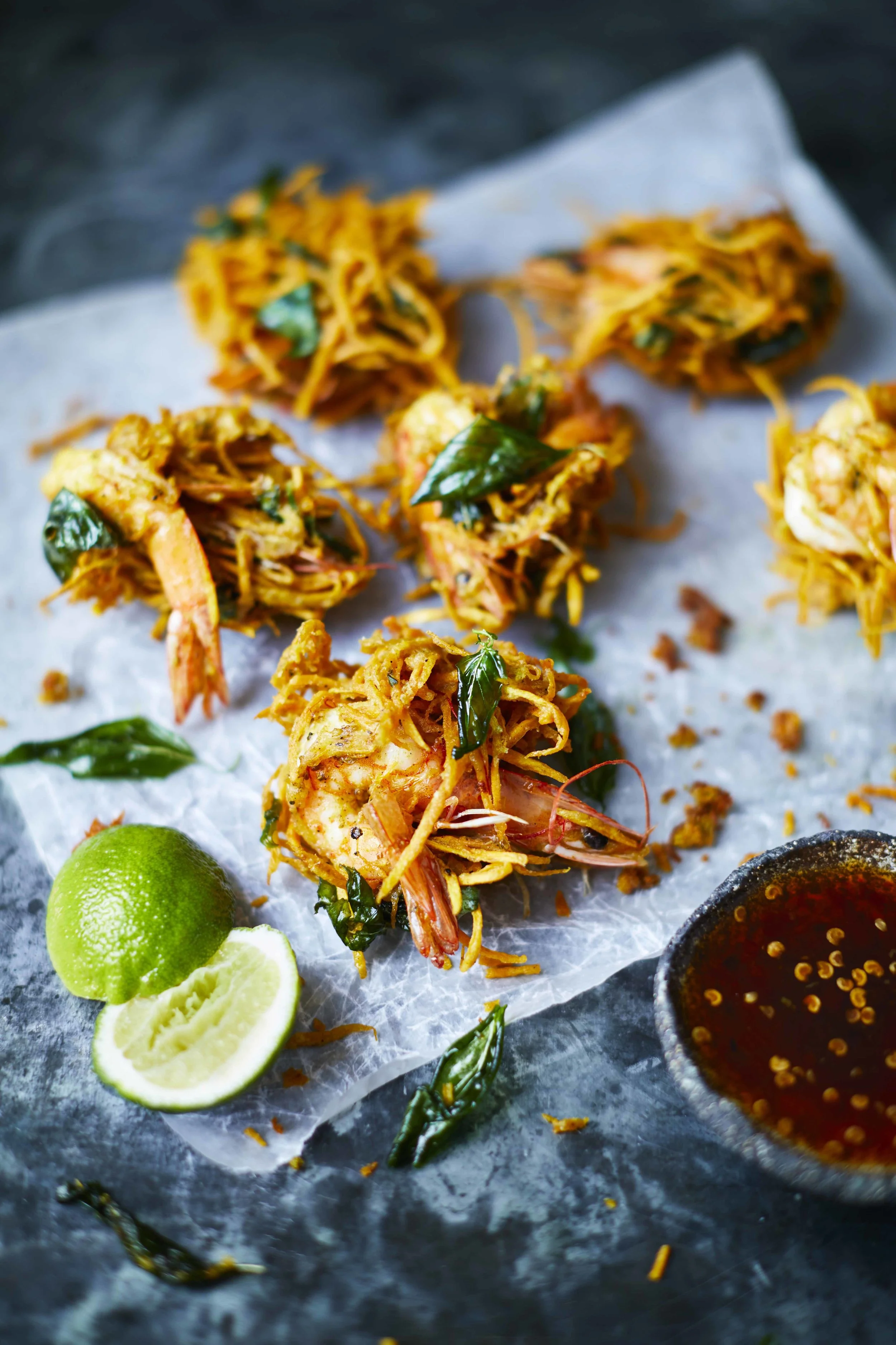 Crispy tiger prawn, sweet potato and daikon fritters with Thai basil on crumpled paper with green nahm jim dipping sauce alongside, recipe by Sebby Holmes