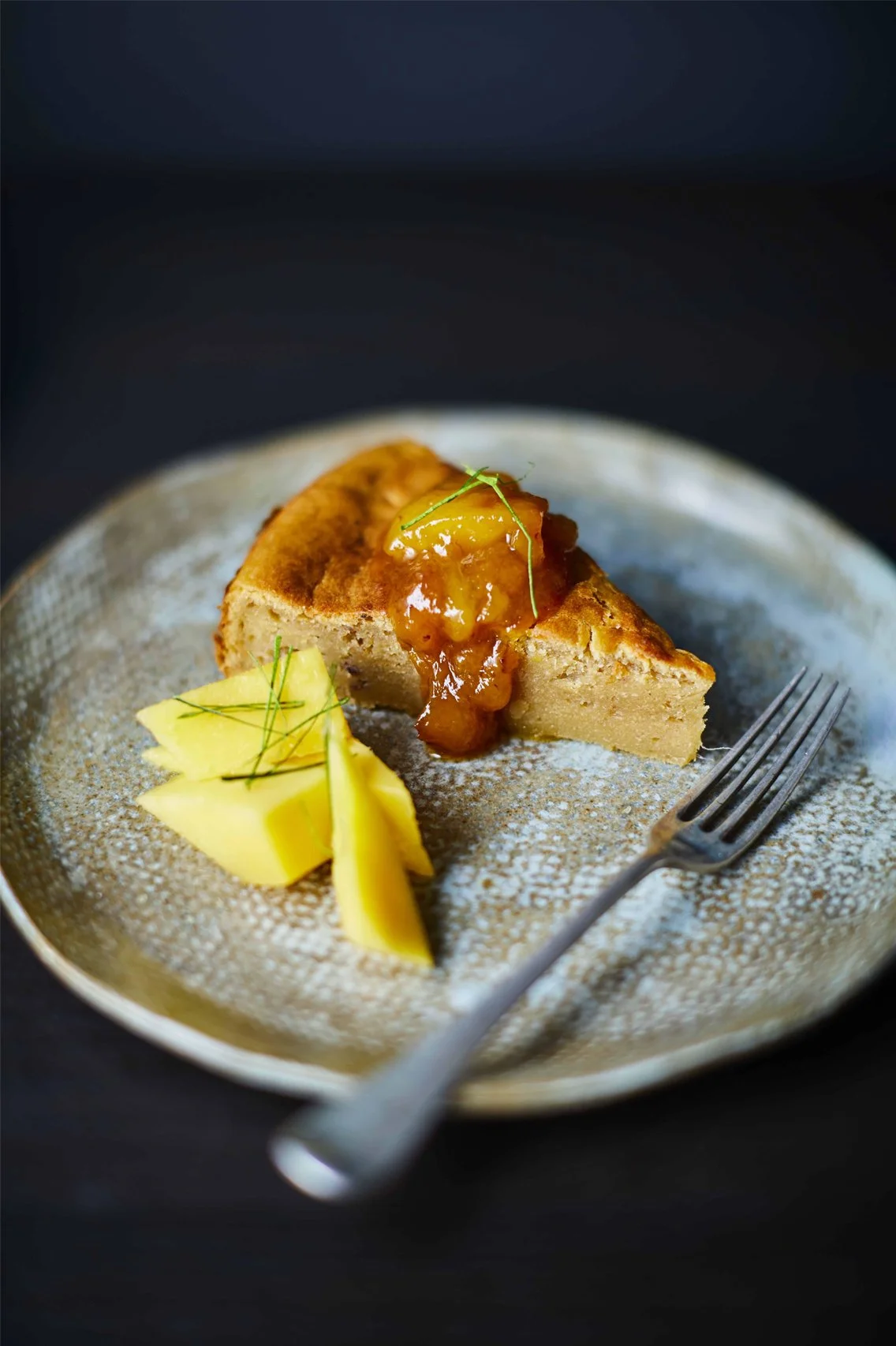 Slice of spiced mango jam cake with mango jam glaze and fresh mango slices on a ceramic plate, recipe by Sebby Holmes