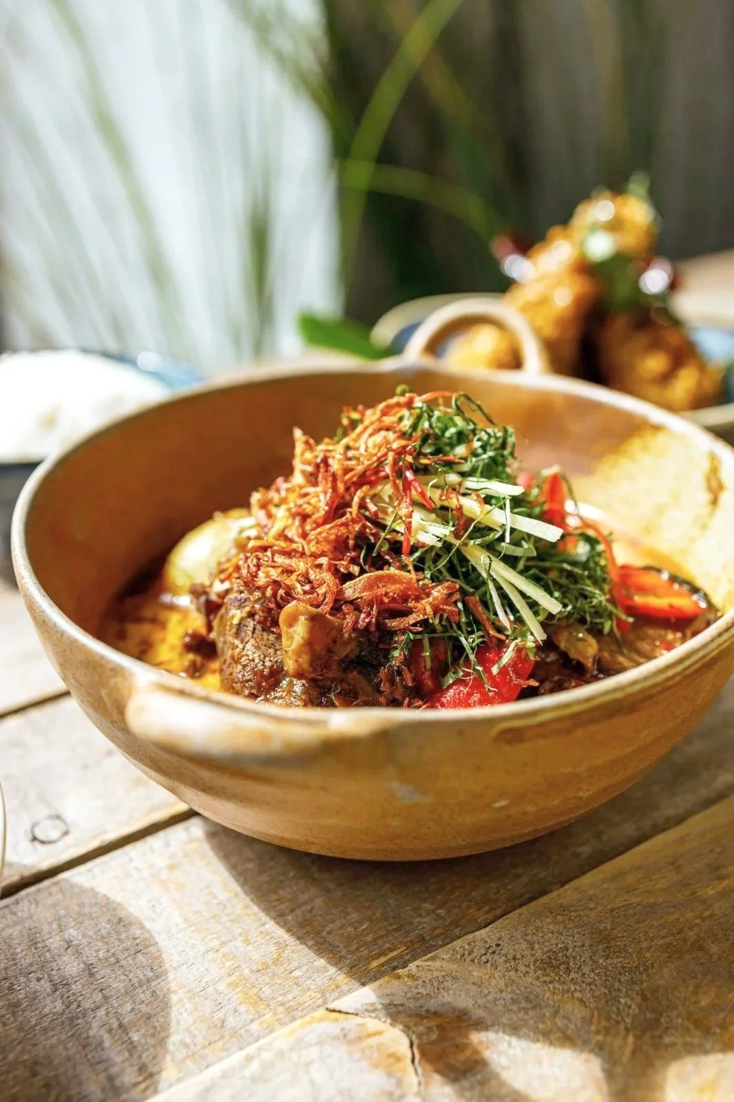 Gaeng gatti beef cheek curry with pickled mustard greens, crispy shallots and sweet basil in a ceramic bowl, recipe by Sebby Holmes