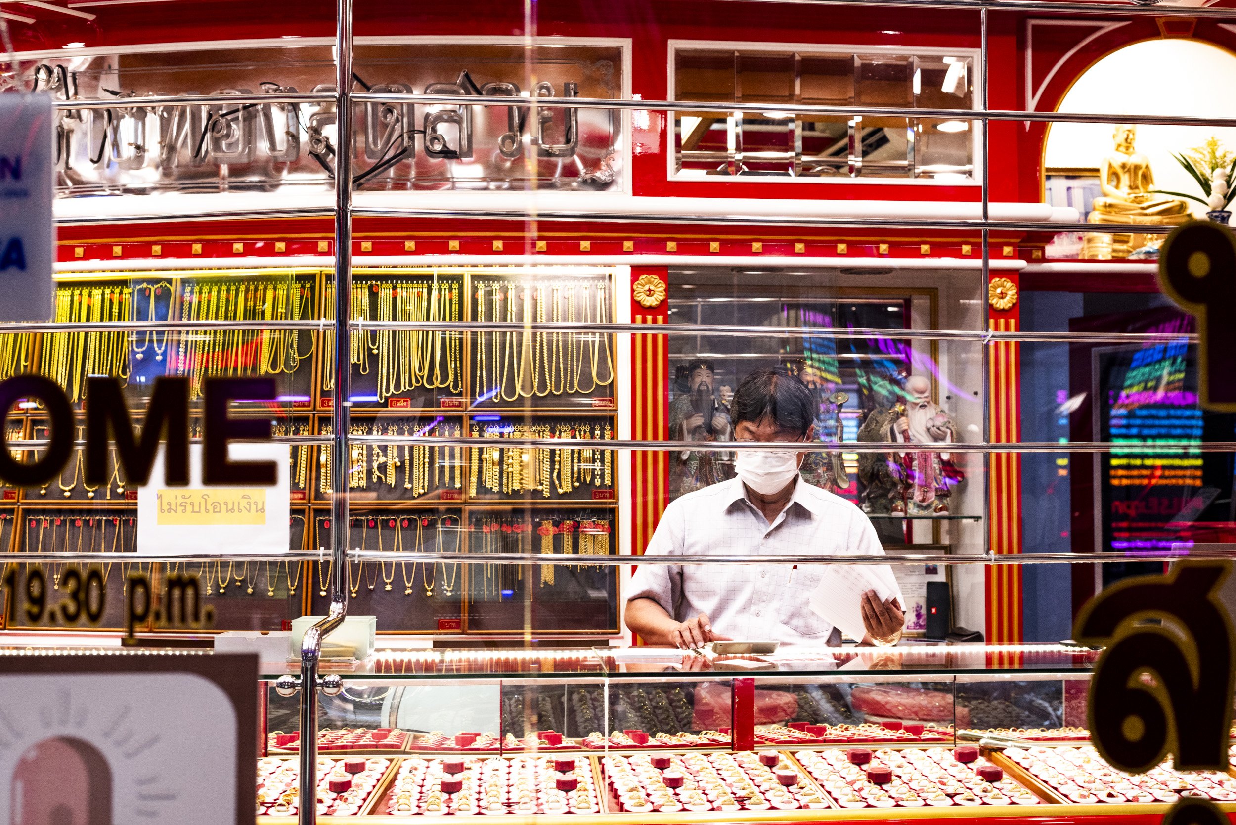 A gold jewellery vendor behind a glass counter in Bangkok, photographed on a Farang trip to Thailand, by Sebby Holmes.
