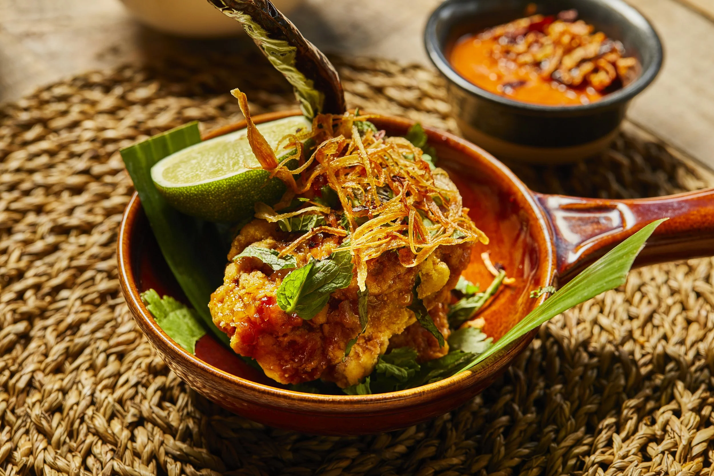 Crispy beer battered chicken Gai Prik with fish sauce glaze, crispy shallots, fresh chilli and herbs on a plate