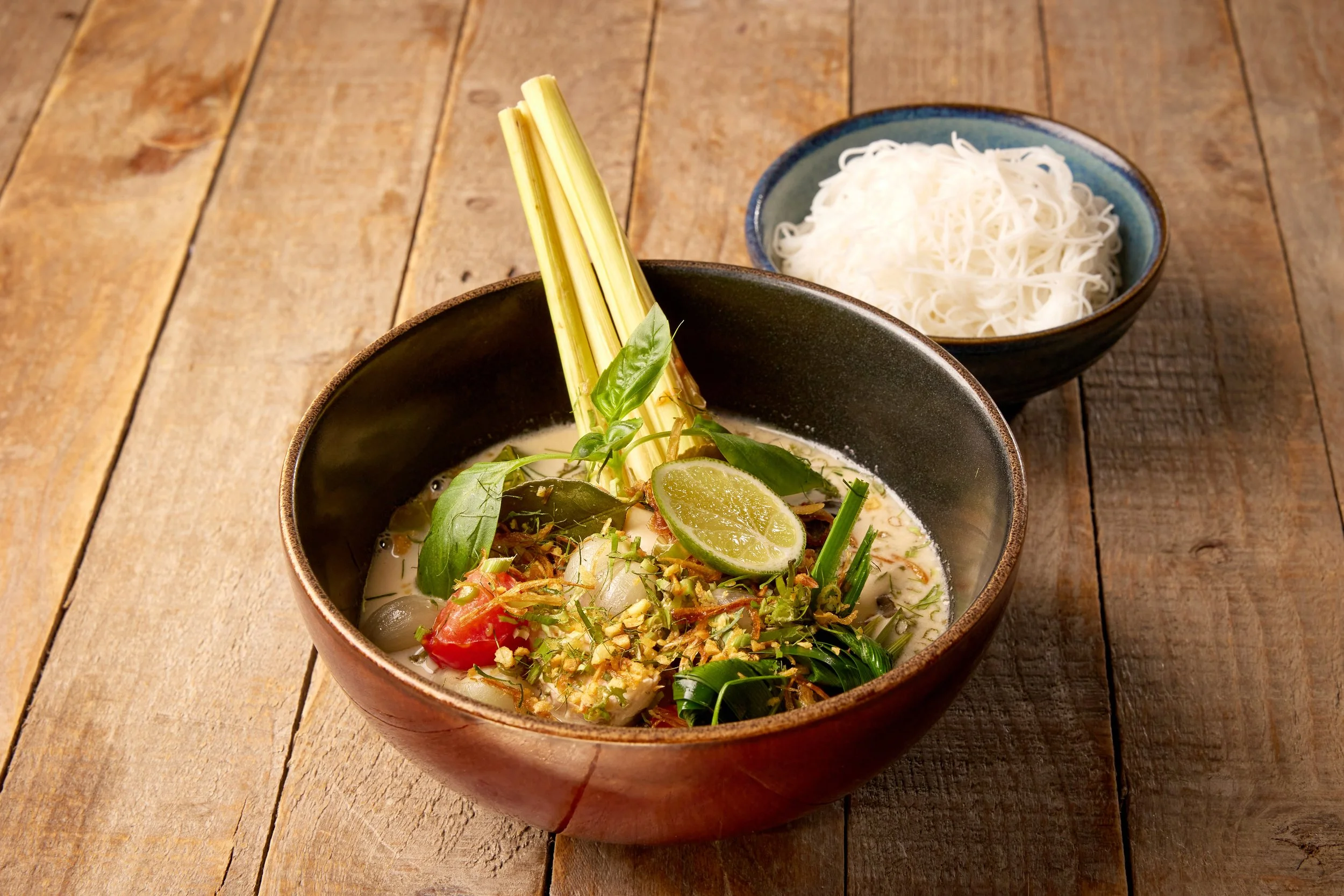 Chicken coconut and galangal rice noodle soup with Thai basil, crispy shallots and lime in a bowl