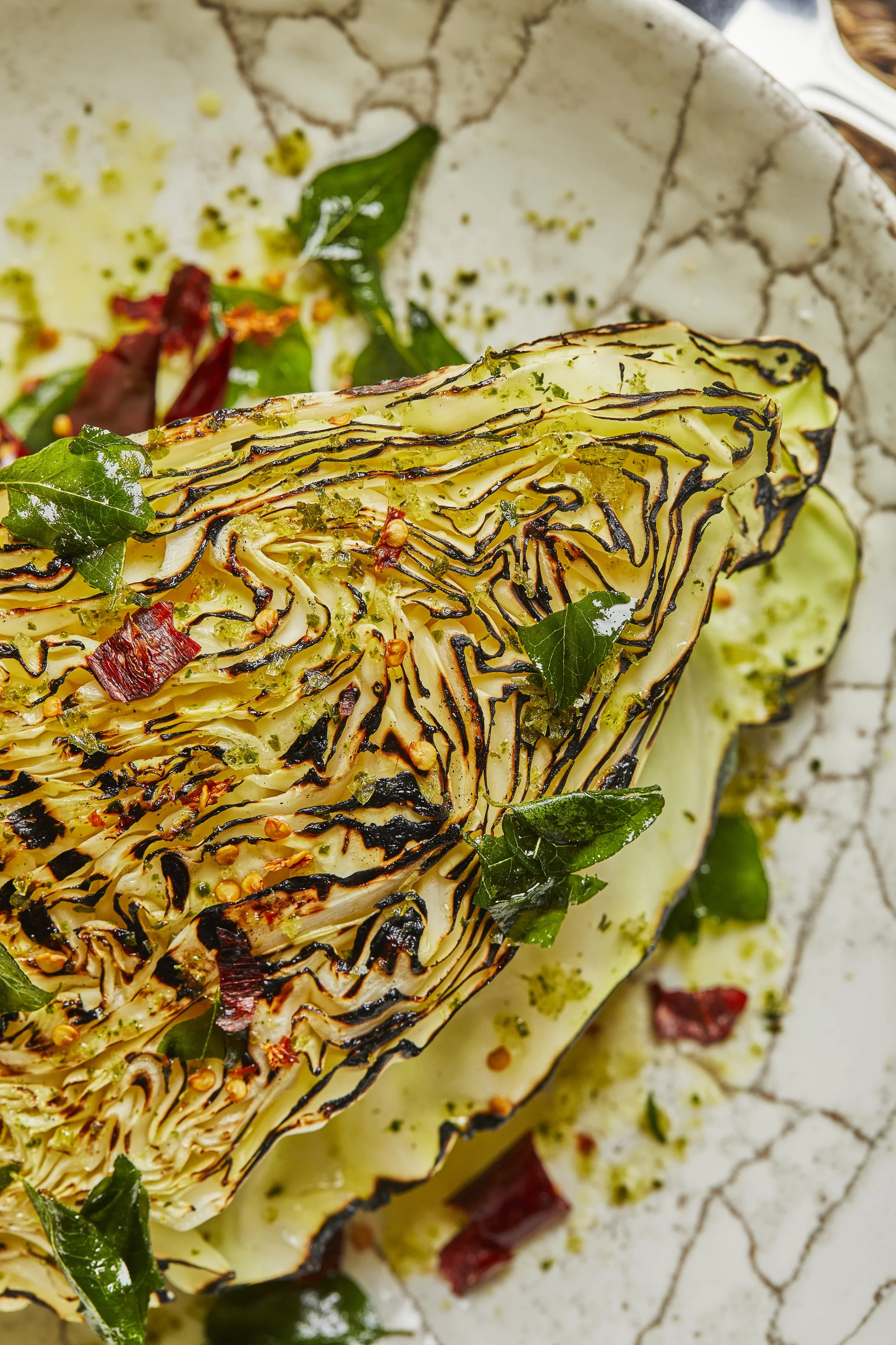 Charred hispi cabbage with turmeric gapi butter, crispy shrimp floss, curry leaves and fresh herbs on a serving plate