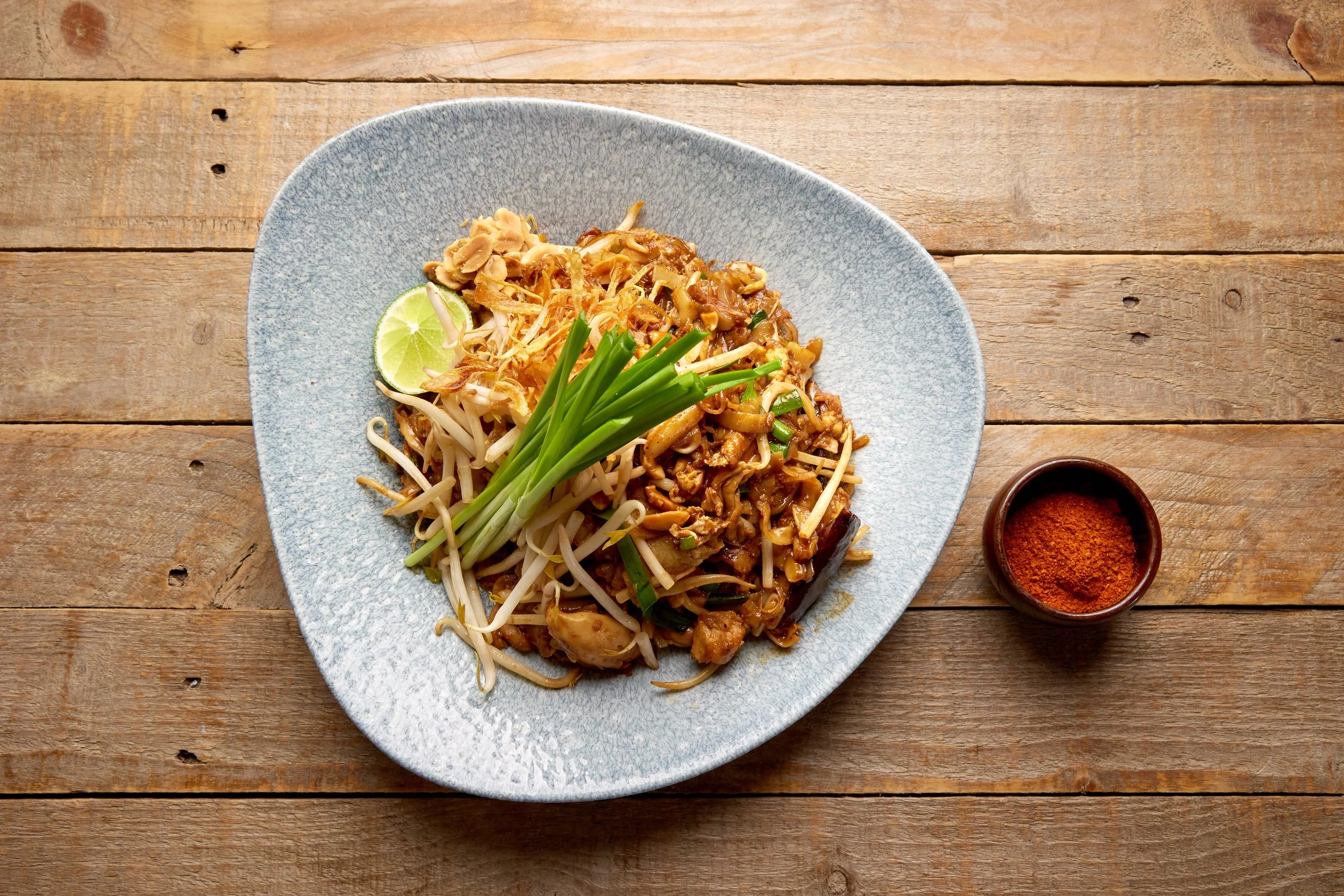 Crab and smoked chicken pad Thai noodles with beansprouts, Chinese chives, peanuts and lime on a large plate