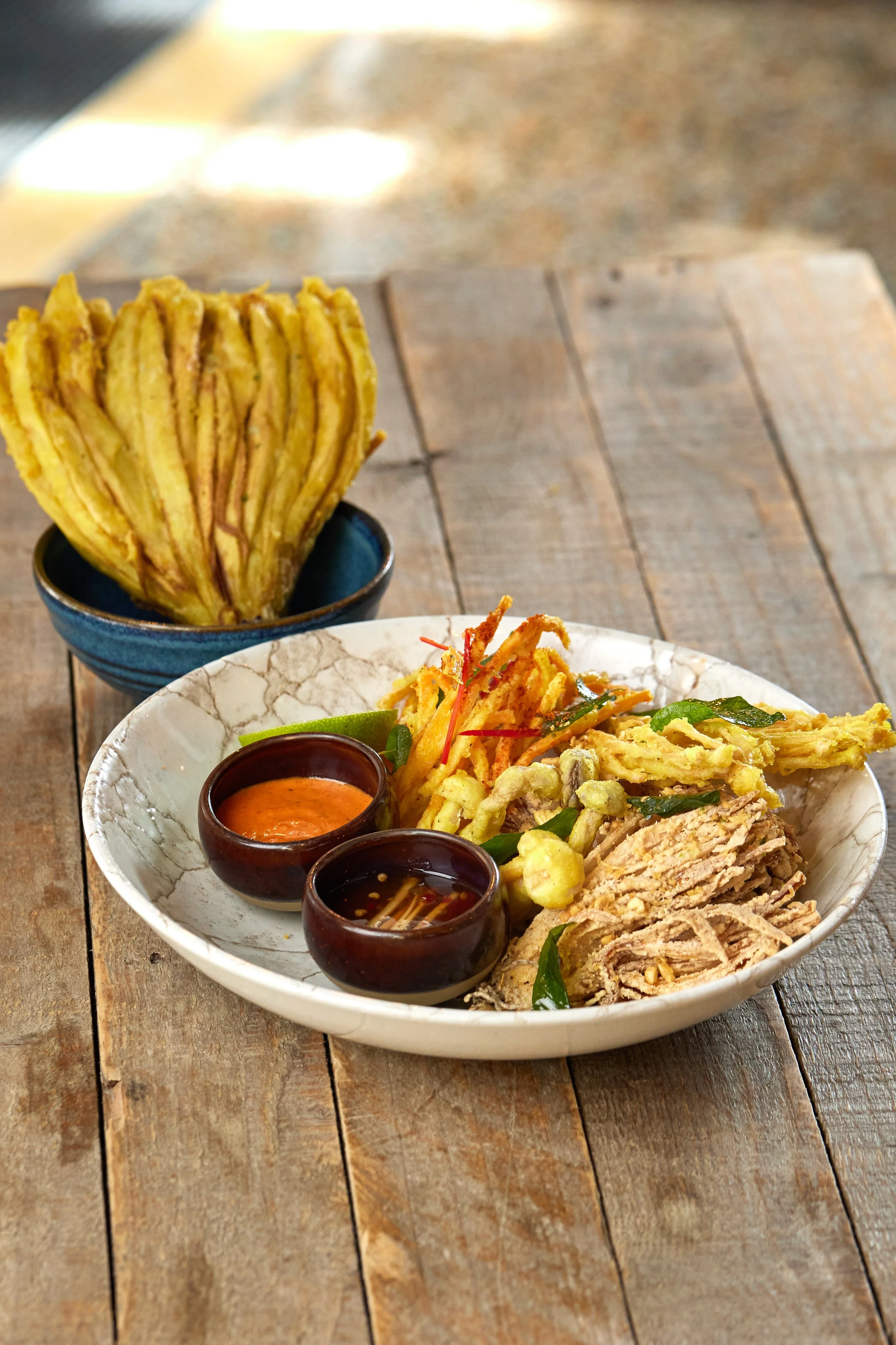 Crispy Singha beer-battered tempura vegetables with crispy curry leaves, chilli powder and dipping sauce on a sharing plate
