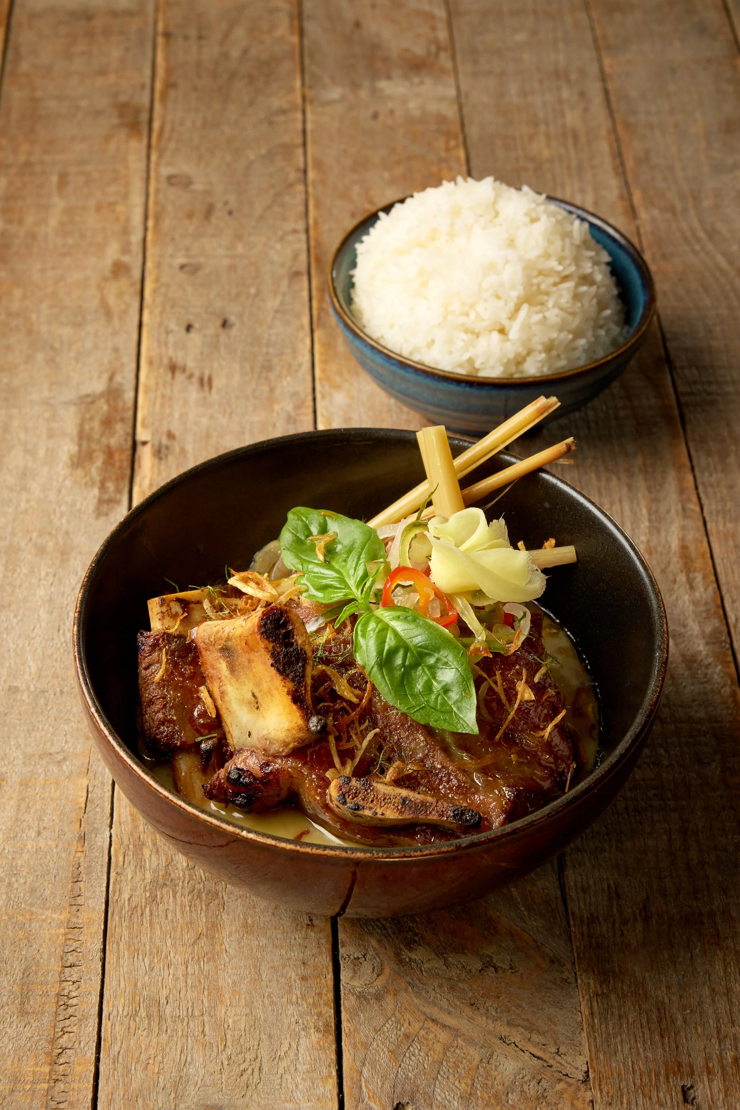 Coconut braised beef short ribs with pickled ginger, cucumber, crispy shallots and Thai basil in a bowl with jasmine rice
