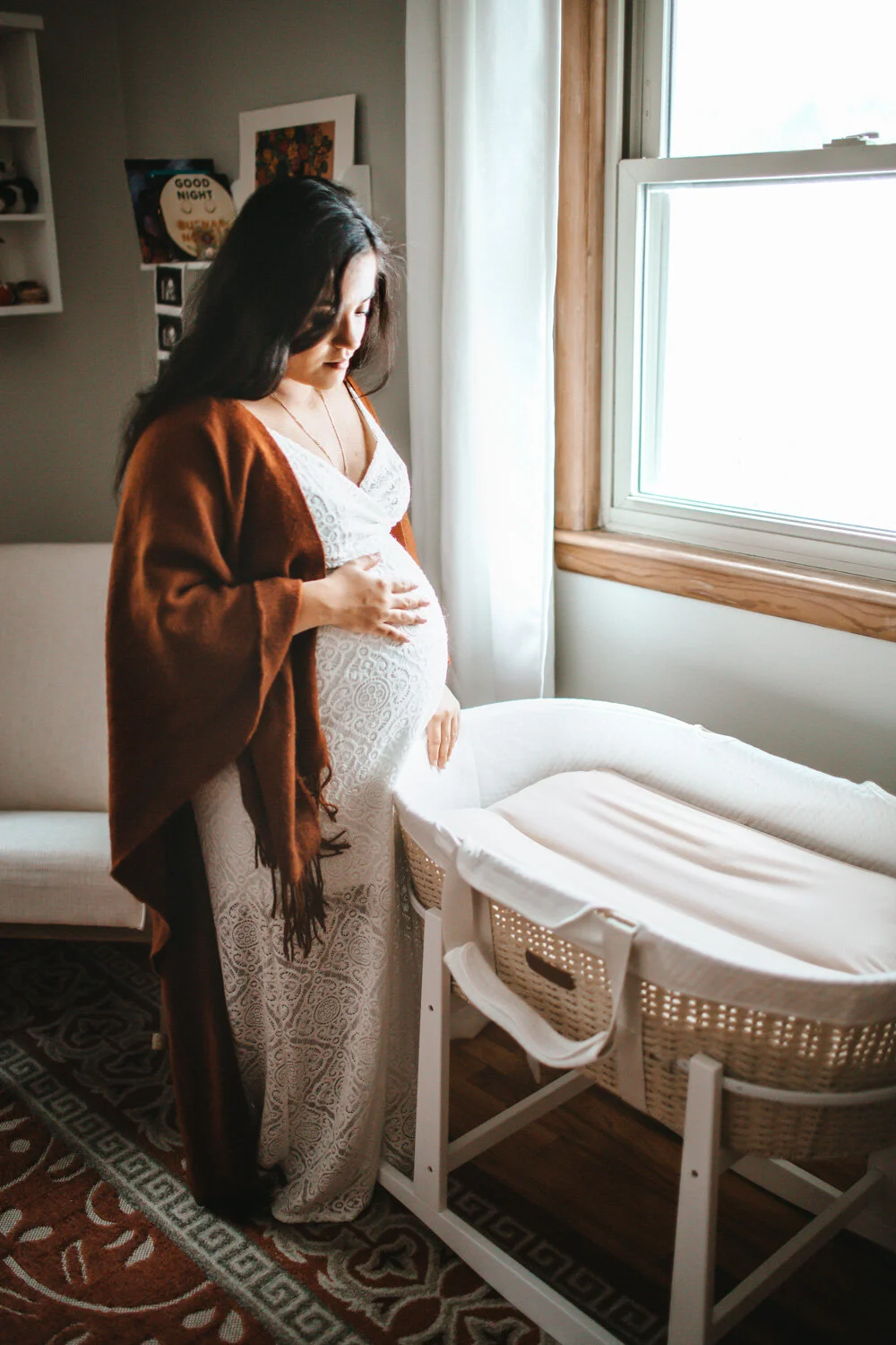 Expecting mother holding belly standing by crib, sunlight streaming in through window