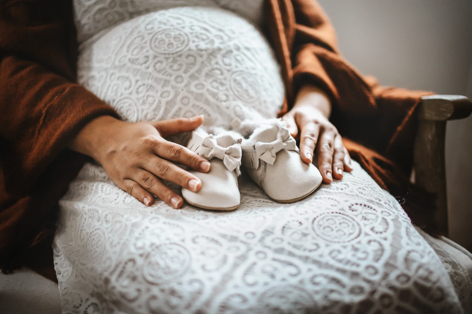 Expecting mother sitting down in nursery holding newborn shoes