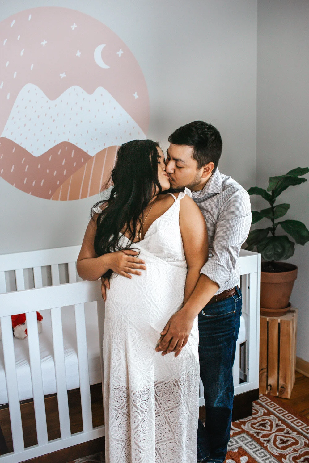 Expecting mother leaning against partner standing in baby's nursery, sunlight streaming in through window