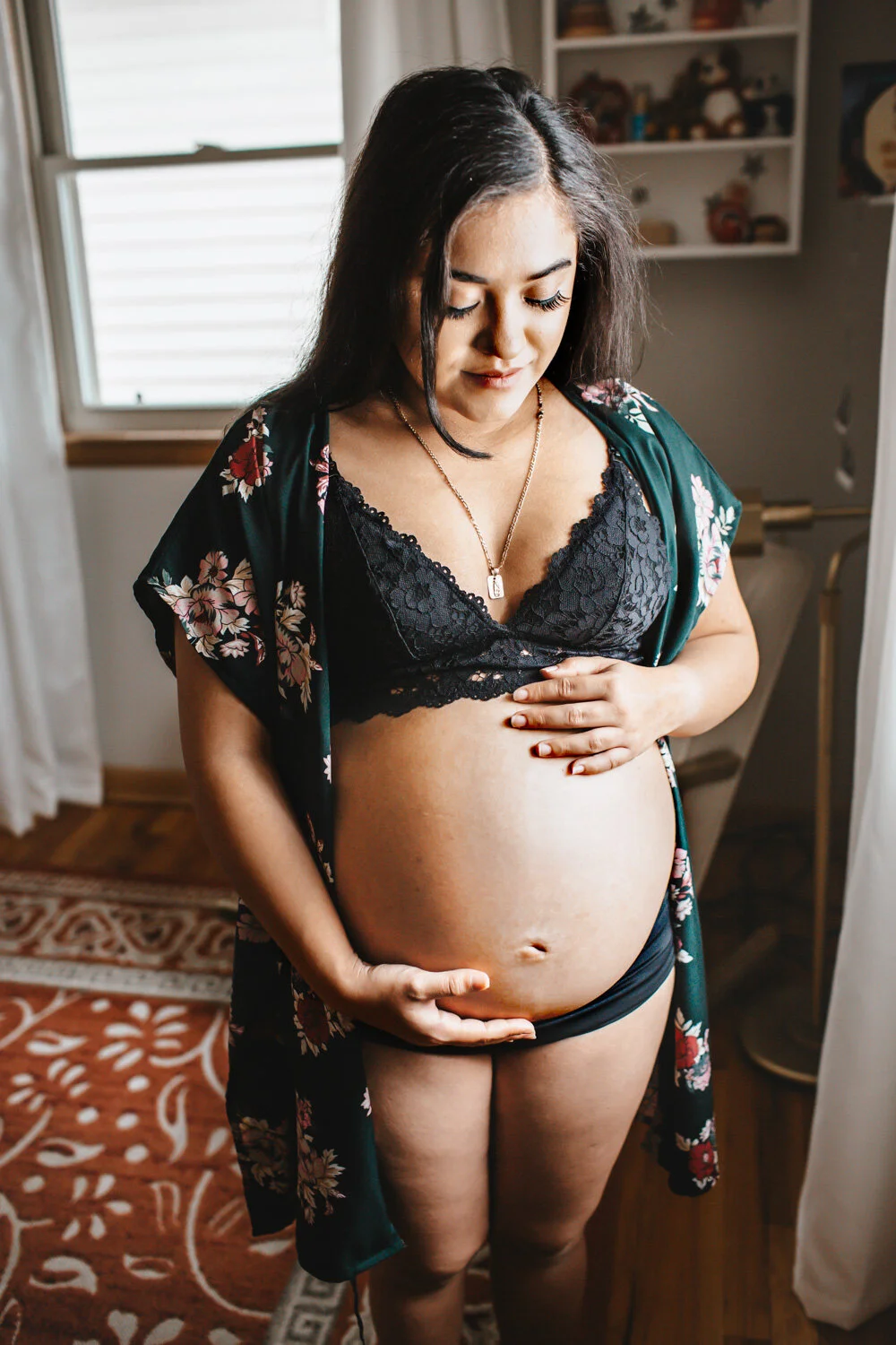 Expecting mother holding belly standing in baby's nursery, sunlight streaming in through window