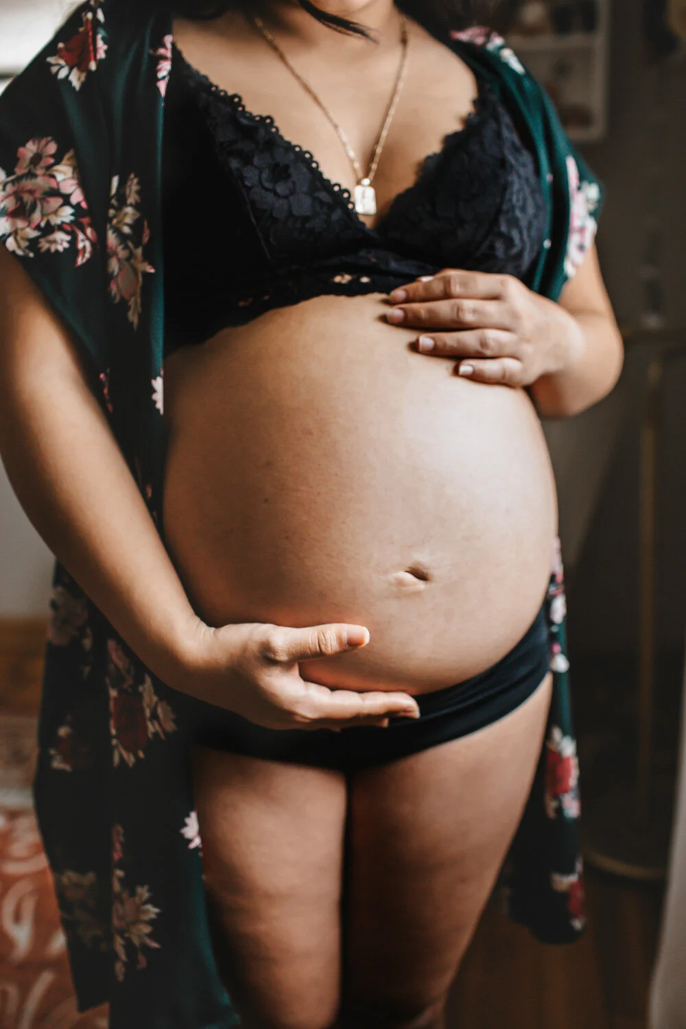 Expecting mother holding belly standing by crib, sunlight streaming in through window