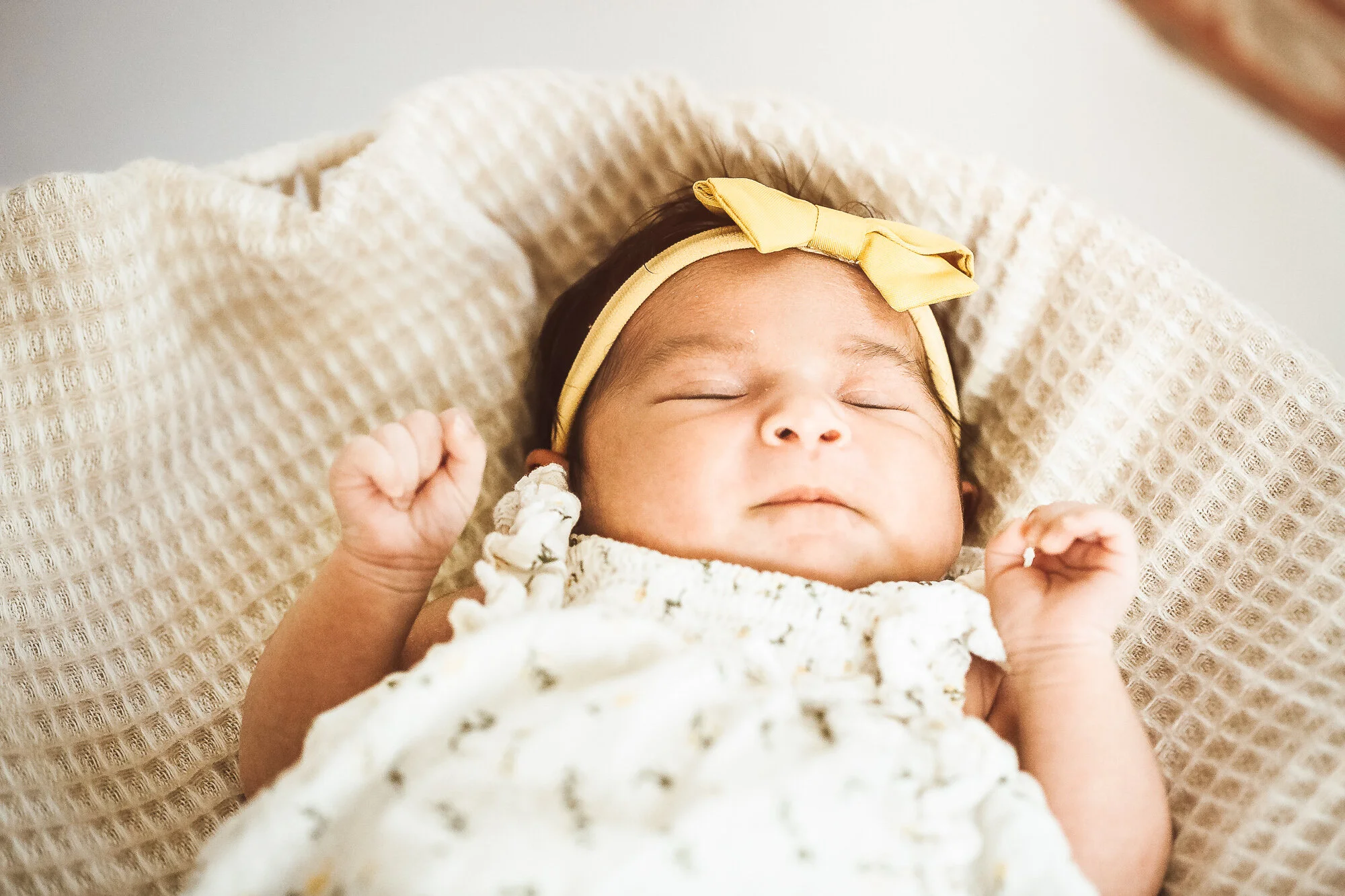 Newborn baby girl laying down with hands by her face