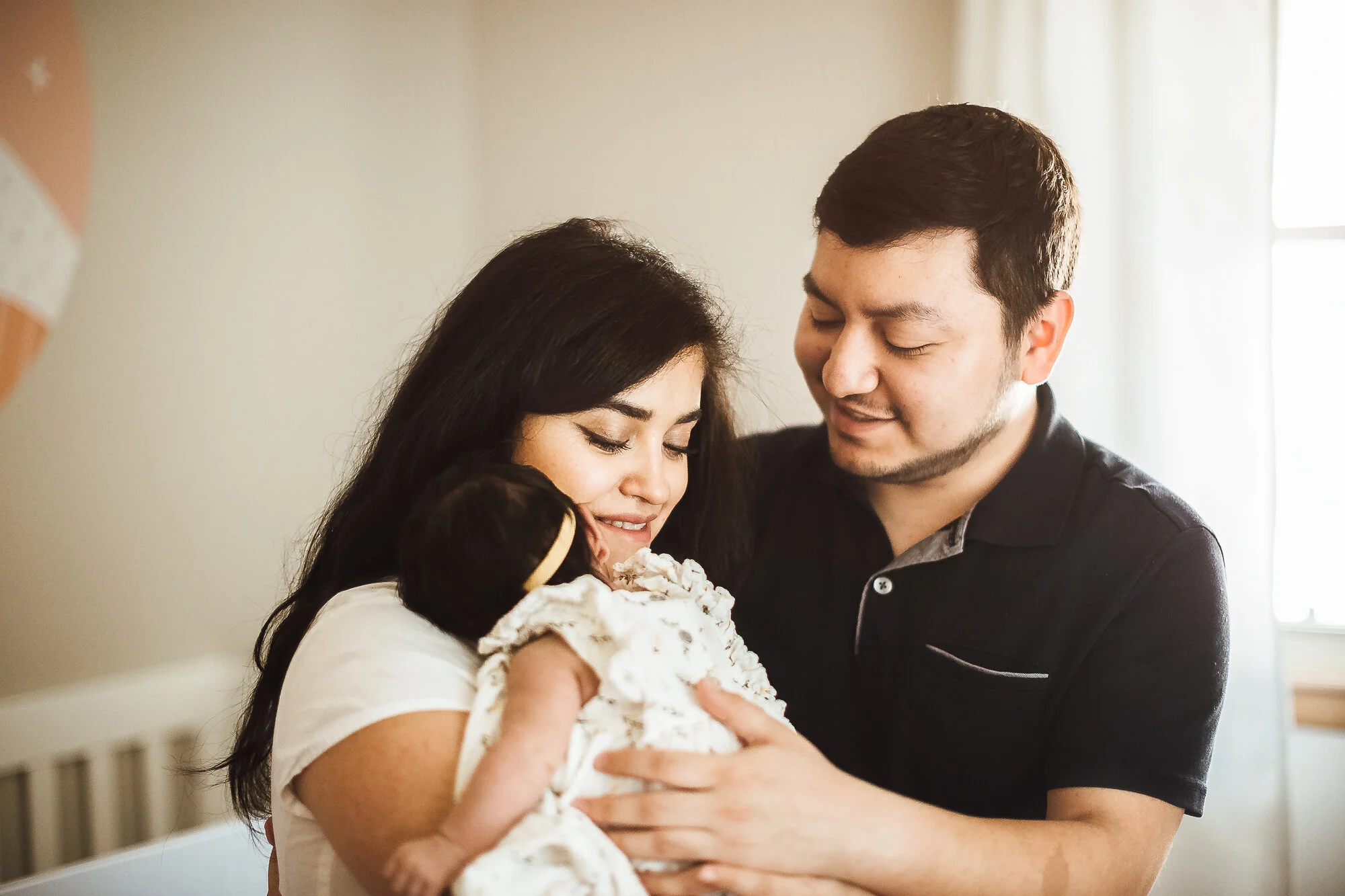 Mother and father snuggling newborn baby girl in nursery