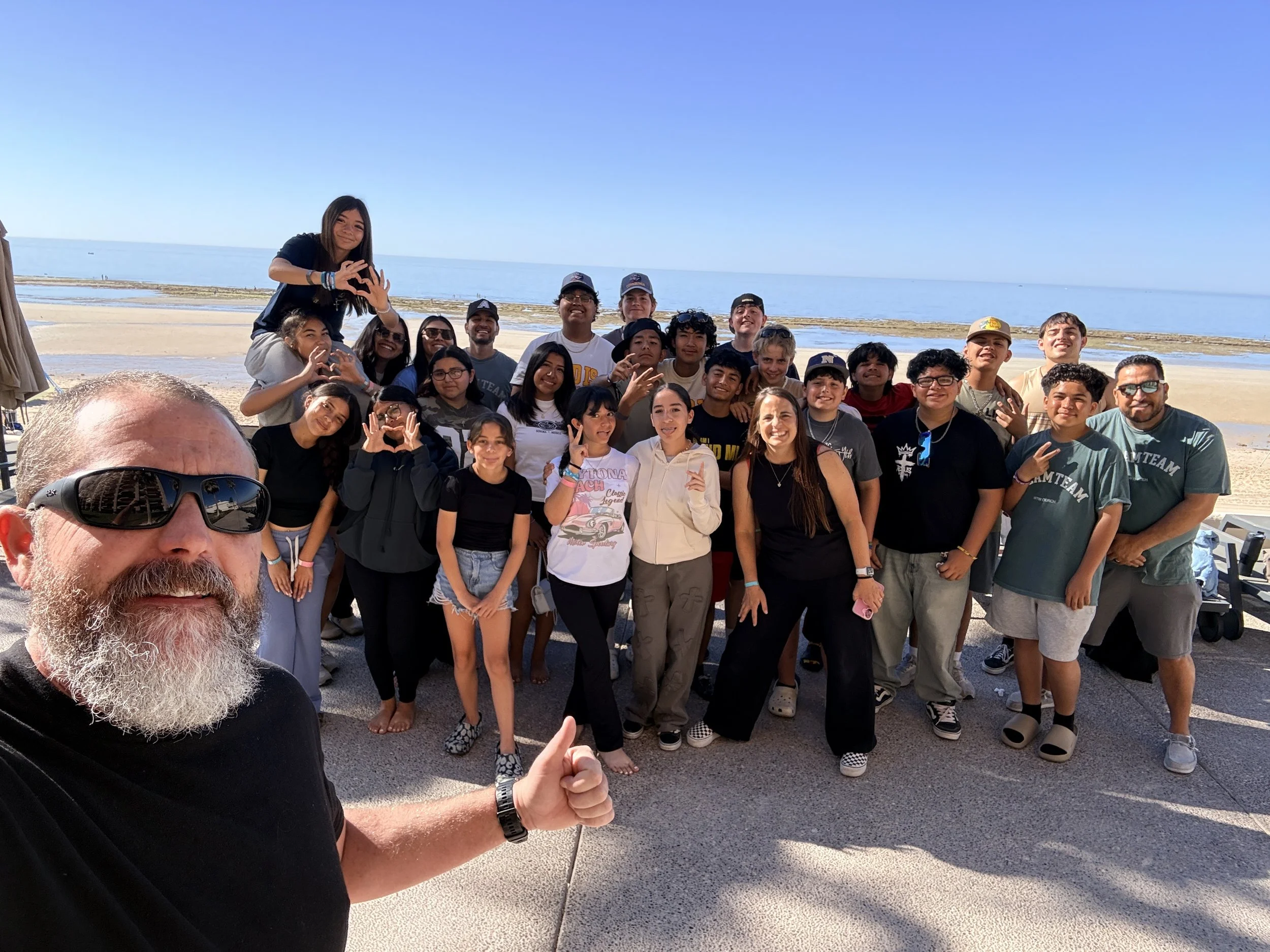 Group of children and teenagers gathered in a parking lot at sunset, smiling and posing for a photo.
