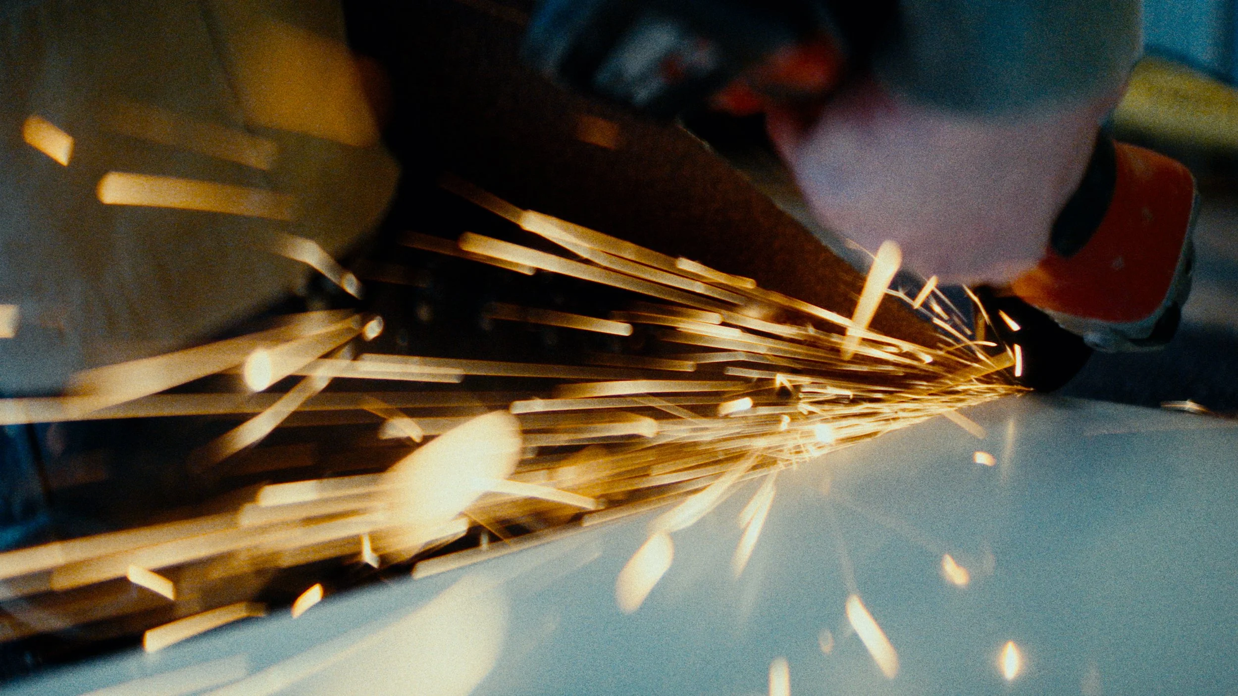 Close-up of a worker grinding metal with sparks flying.