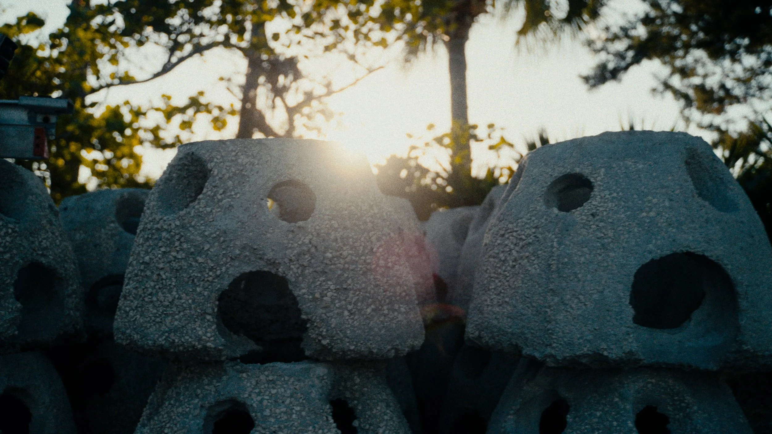 Group of concrete rocks with hollow centers stacked outdoors with trees and sunlight in the background.