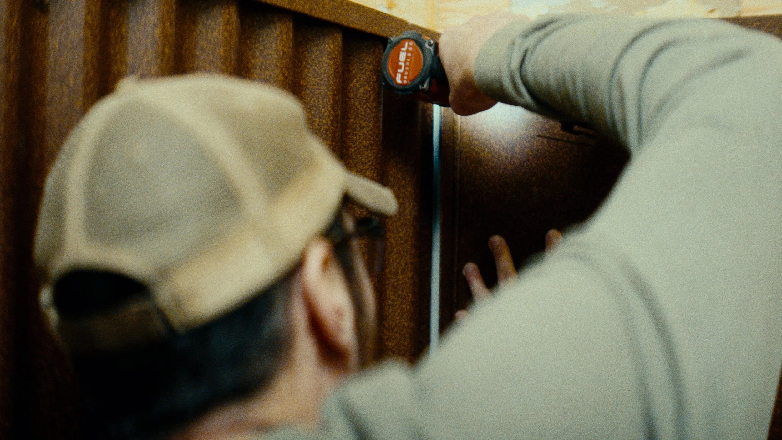 Two children, one wearing a beige cap and the other in a gray long sleeve shirt, leaning over a piece of furniture while a person, whose face is not visible, uses a measuring tape on the furniture.