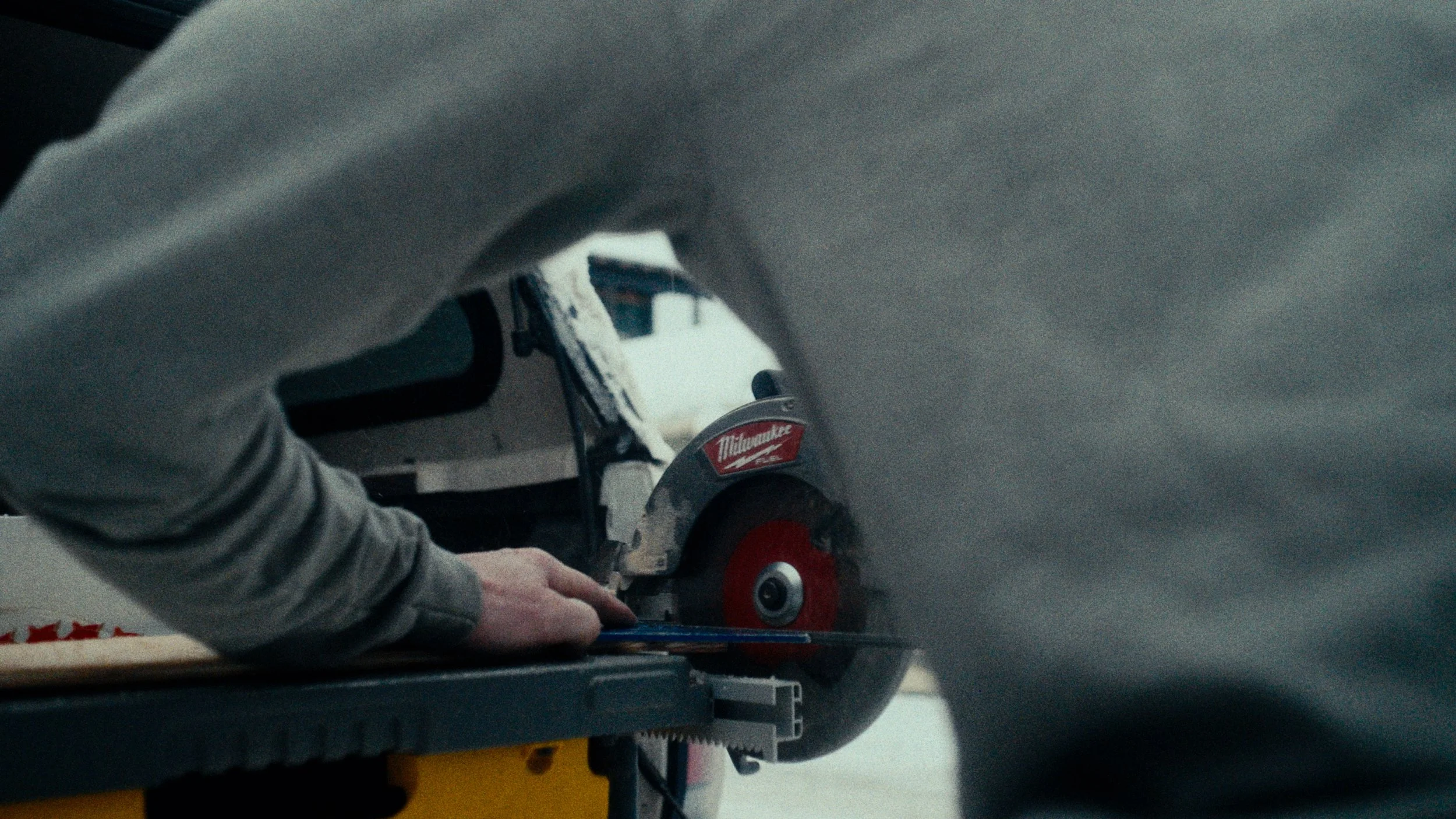 A person operating a Milwaukee circular saw, cutting a piece of material.