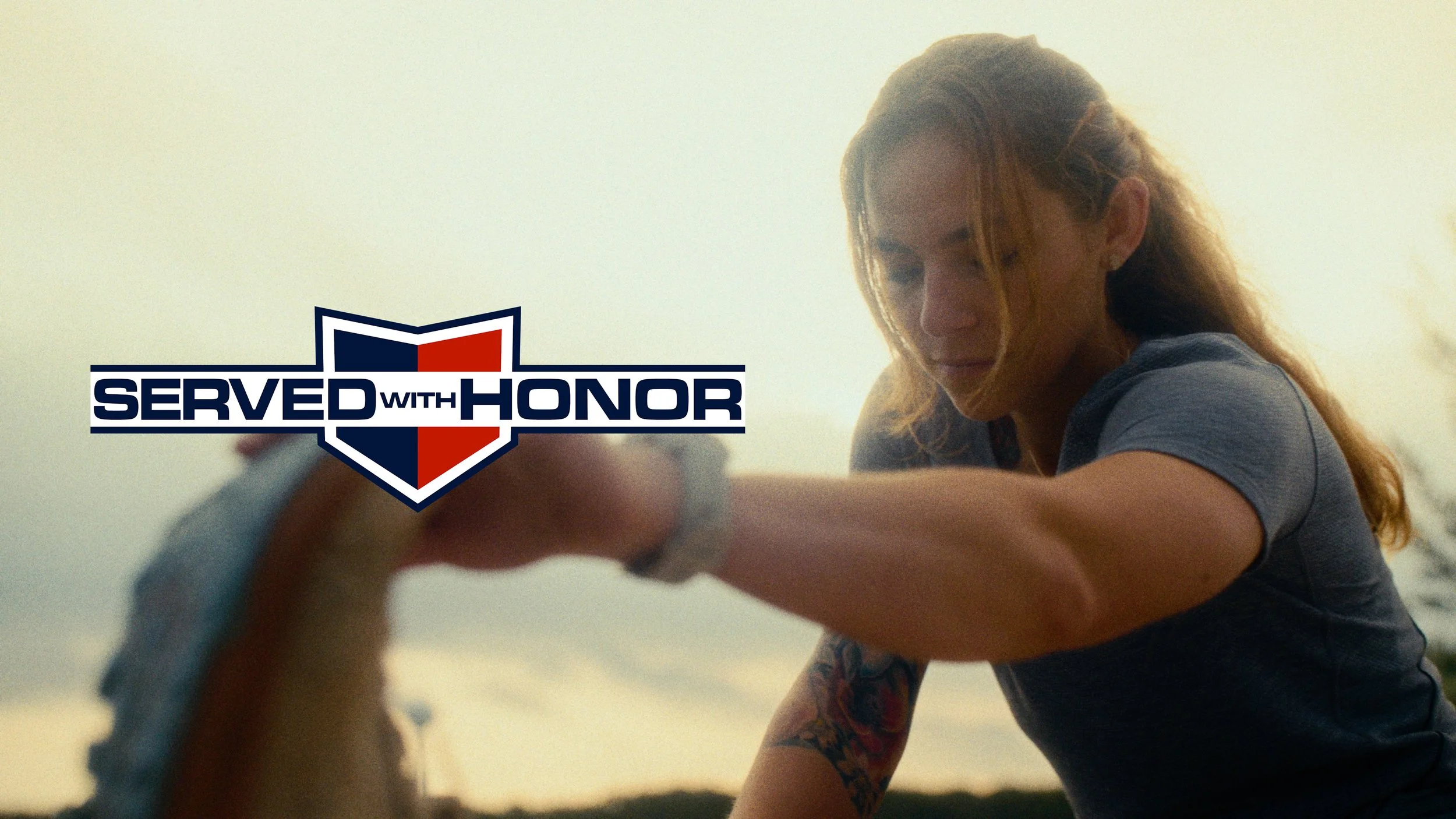 A woman with long hair, wearing a gray shirt, is reaching out her hand while outdoors during sunset. A logo with a shield and the text 'Served with Honor' is overlaid on the image.