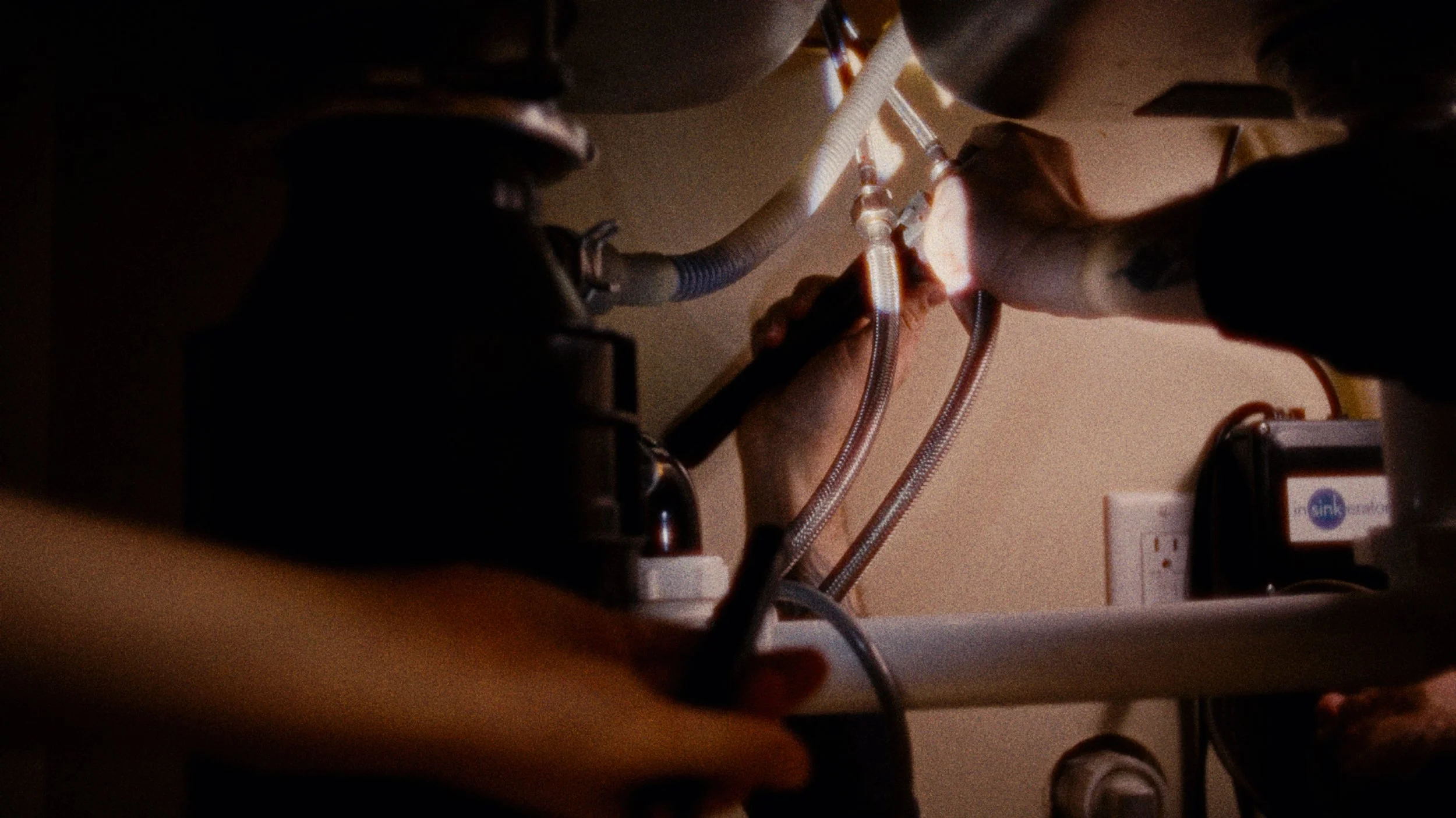 Person at a medical or technical workspace handling wires and equipment, with a focus on hands and tools in a dimly lit environment.