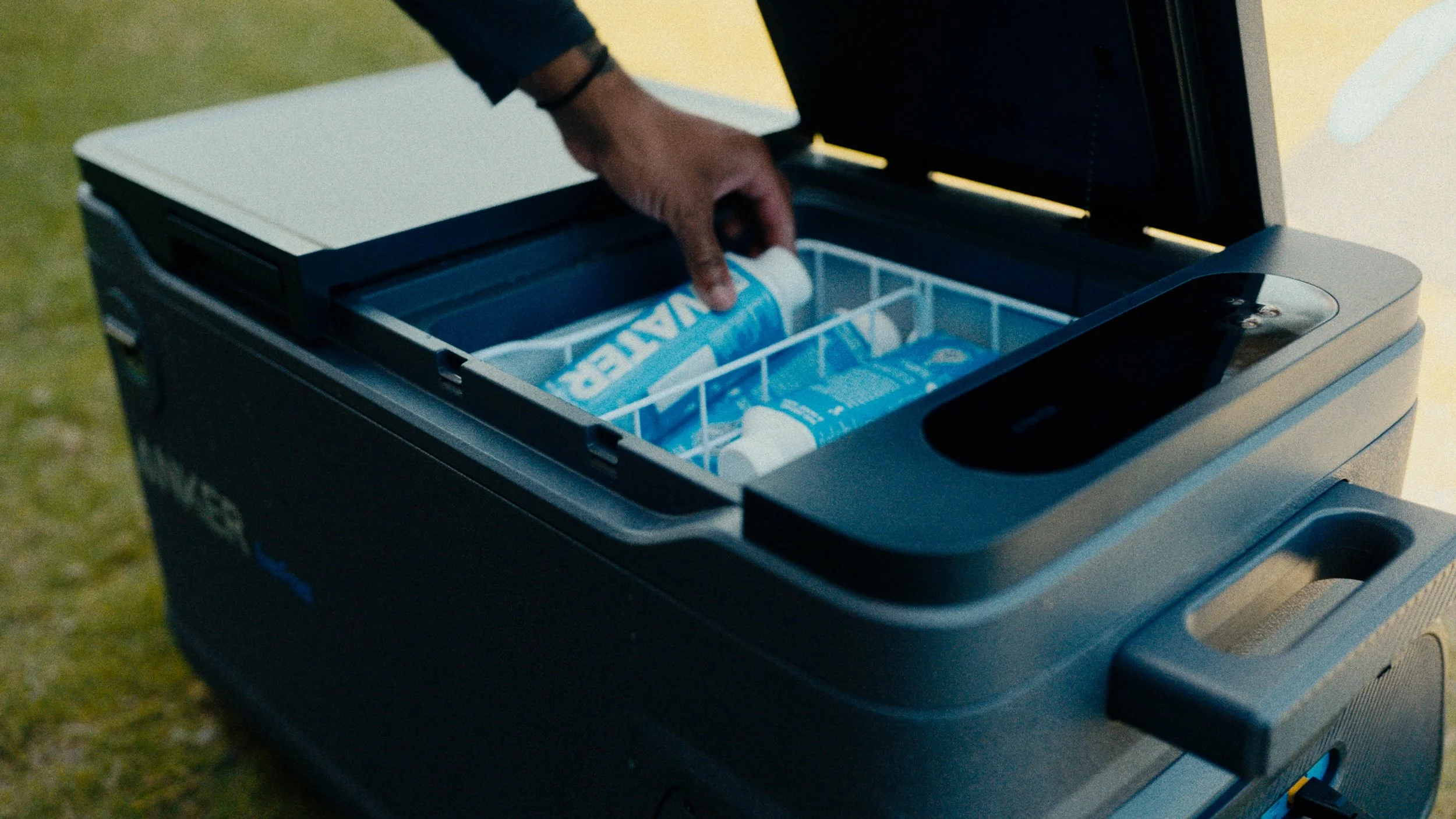A person is placing bottles of water into a portable cooler or ice chest outdoors.