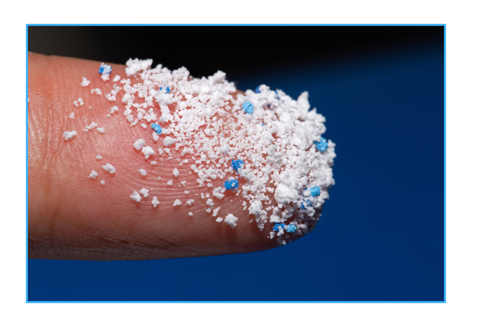 Ein Finger in Nahaufnahme auf dem winzige Plastikteilchen zu sehen sind