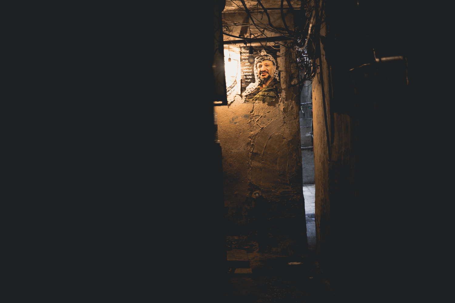  A lone light bulb illuminates a photo of Yassar Arafat.  