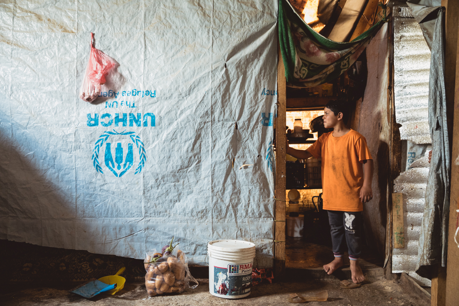  A young boy waits for his turn to wash himself inside the tent he and his family live in.  