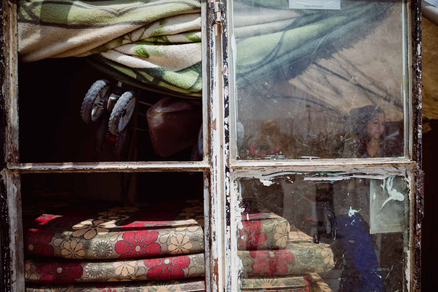  An old window leans against the outside of a tent housing a refugee family. 