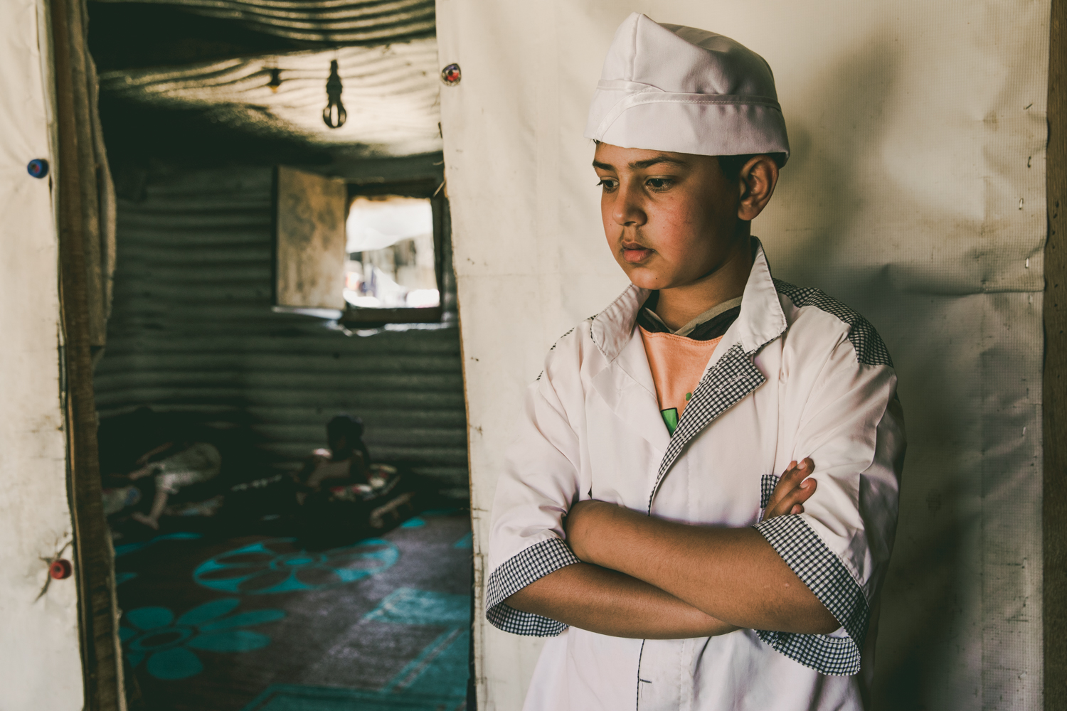  A young boy returning from his work shift stands outside the door to his family’s tent. 