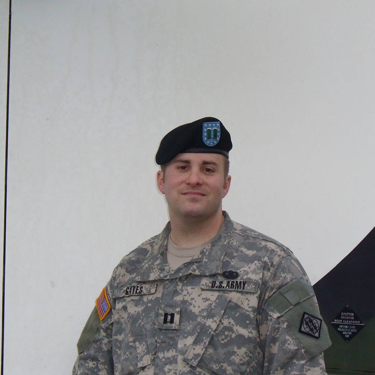 A person wearing a U.S. Army uniform with a black beret, standing in front of a plain background.
