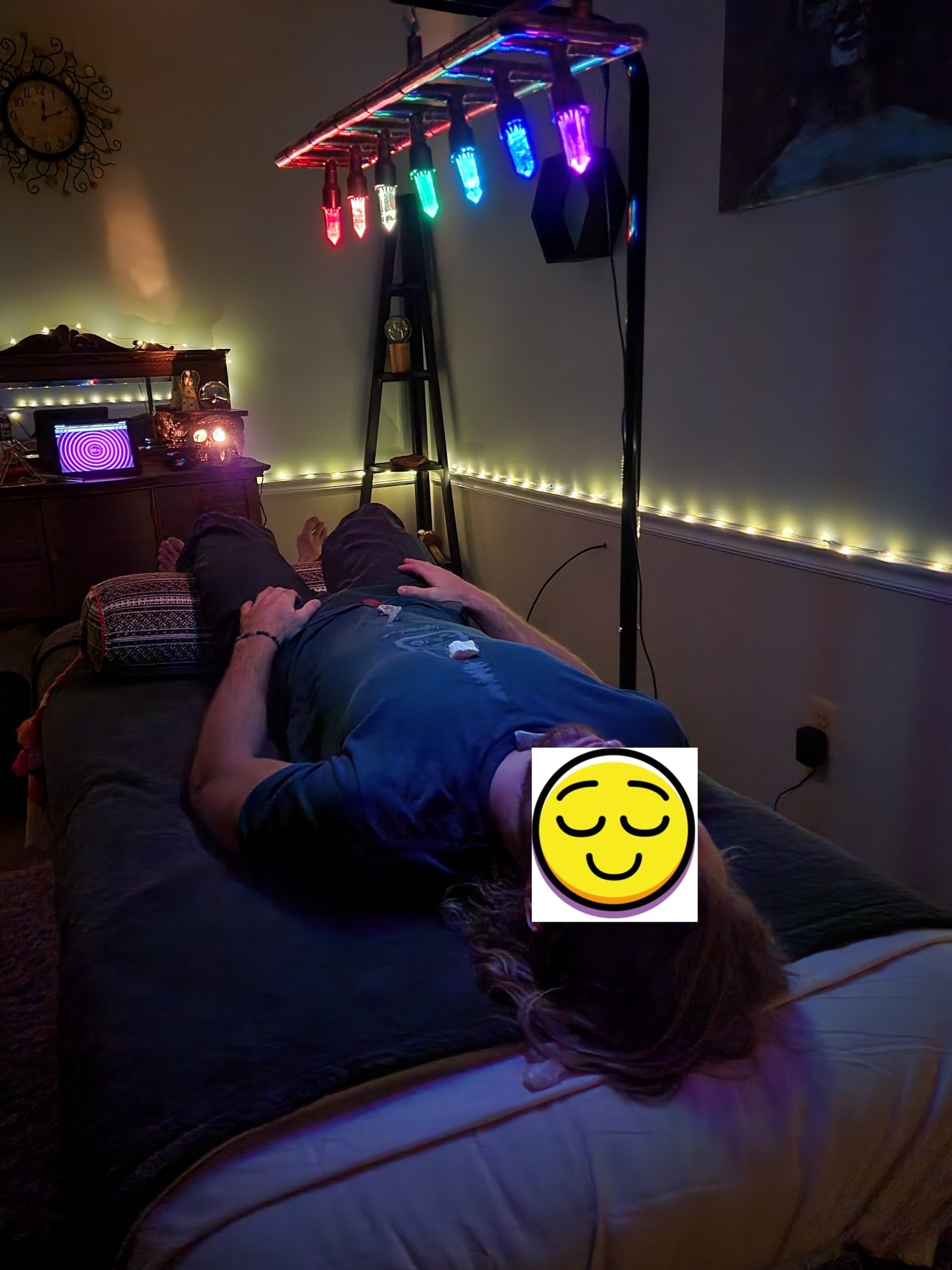 Person lying on a table under colorful LED lights in a dimly lit room, used for relaxation or therapy.