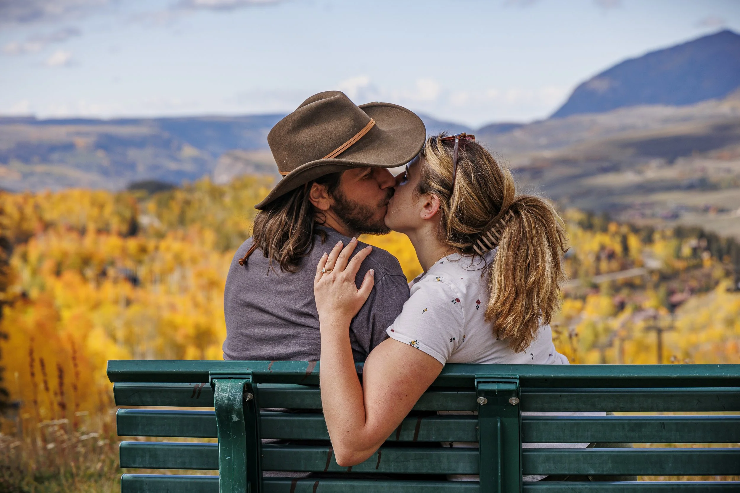 Couple kissing on a bench with scenic autumn landscape in background