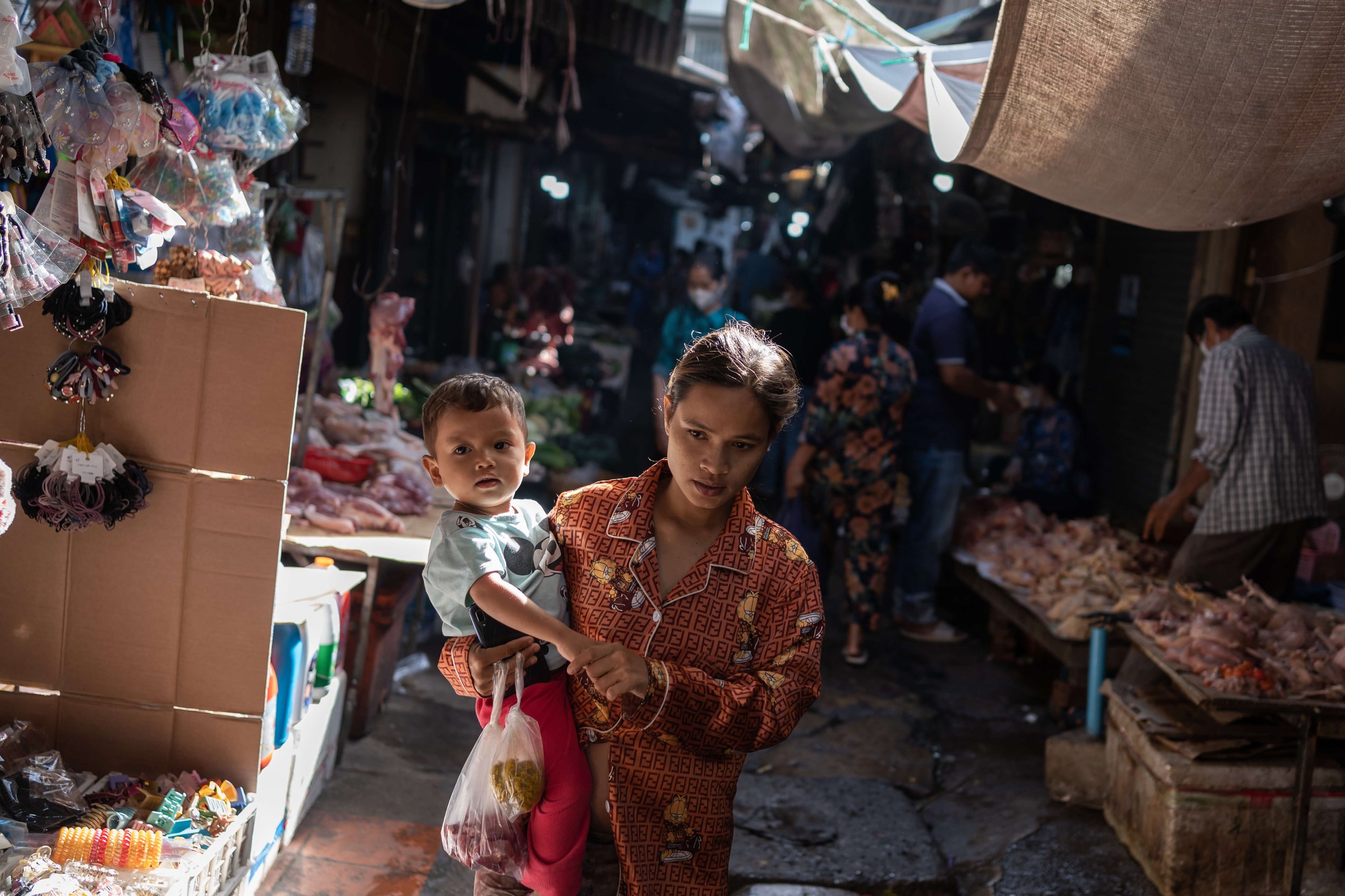  Theary buys food at the local market with her son. As of January 2022, she was six months pregnant and unable to work on the site with her husband as a result, instead staying onsite during the day and looking after her son. An estimated 30-33 perce