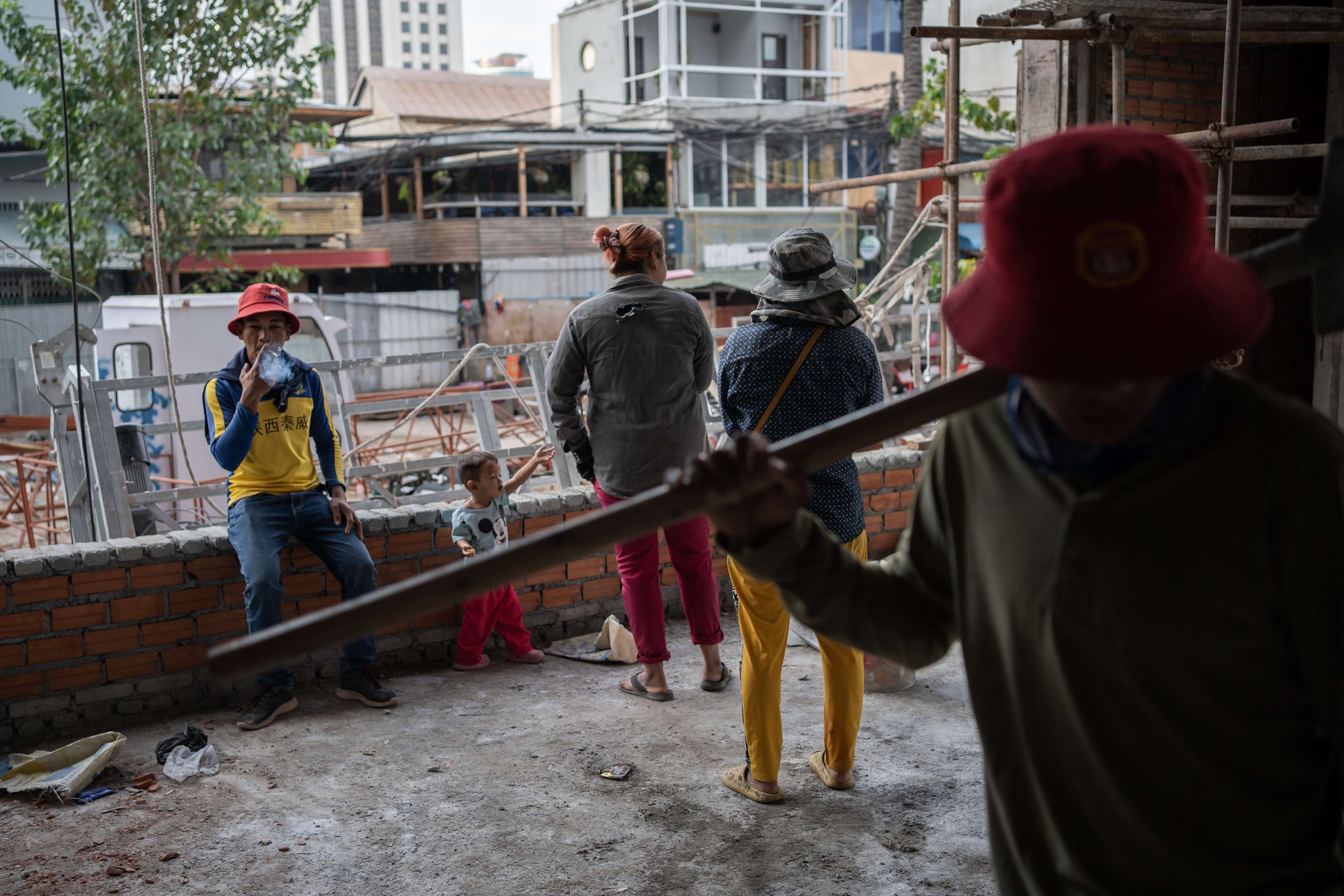  Srieng takes a smoke break with his son and other construction workers on the site. With no other option, his 2-year-old son spends most of his time on the site with his parents or other workers. Srieng also has a daughter from his first wife who li