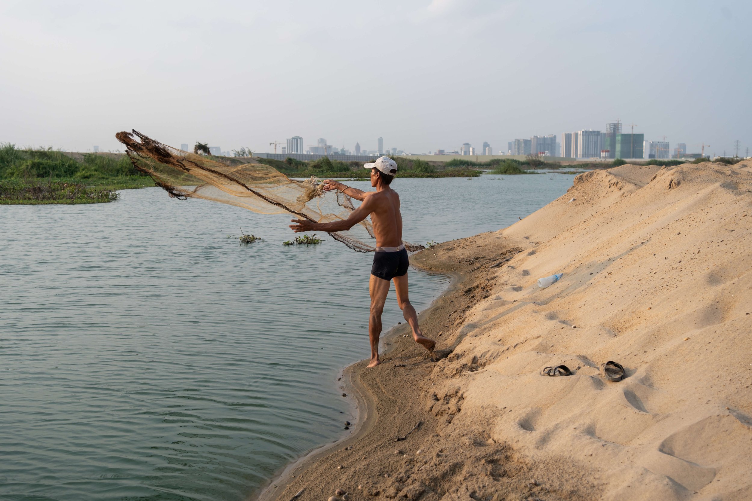  Tayang Sam, a construction worker from Cambodia’s remote Ratanakiri Province, casts his net on sand pumped from the Mekong into the wetlands. Sam has spent the last four years as a bricklayer, constructing a house owned by a member of the wealthy Ca