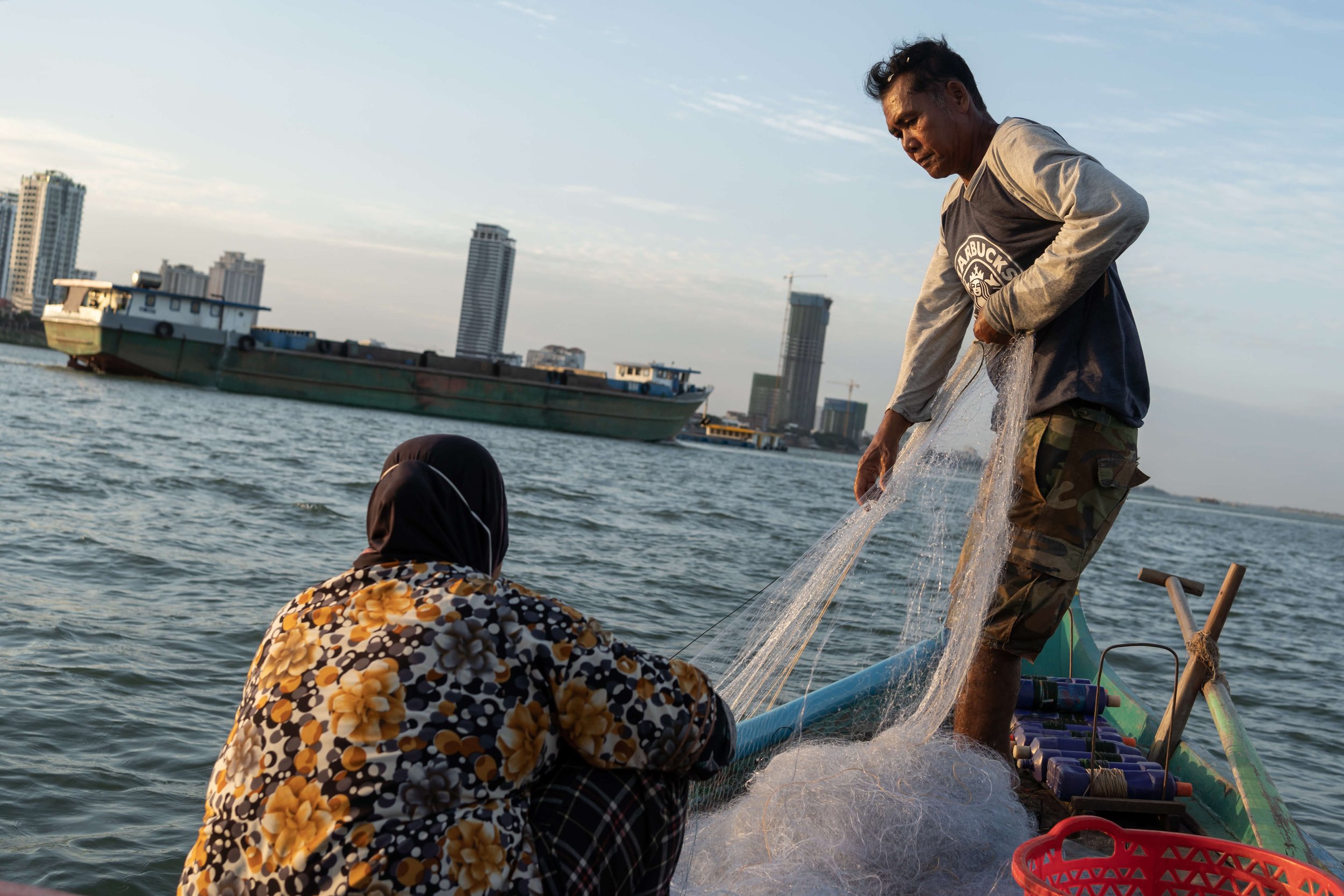  Om Vi (right) and Chip Srey Vas pull up their nets as a sand dredger drives past. They are one of 600,000 Cham people in Cambodia, an ethnic minority considered descendents of the Champa kingdom, who rely on the Mekong River for its fisheries. In 19