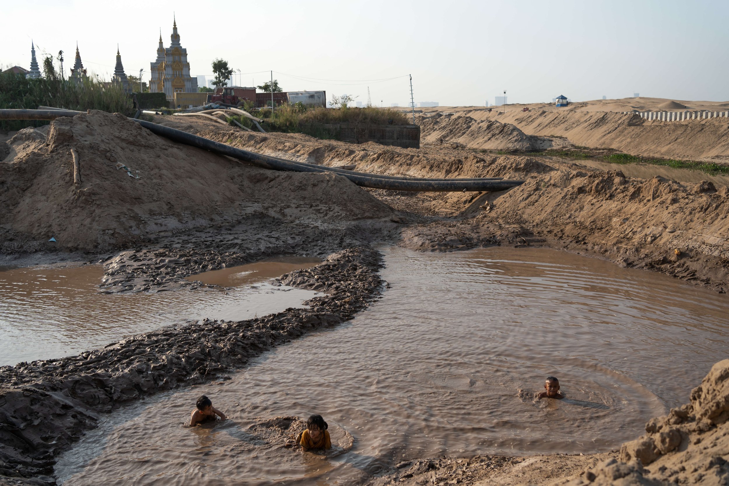  Children play in puddles at a sand deposit site on the outskirts of Phnom Penh. In the background a Buddhist temple sits in front of Koh Norea, a new reclamation project on the Mekong. (Andy Ball/University of Southampton) 