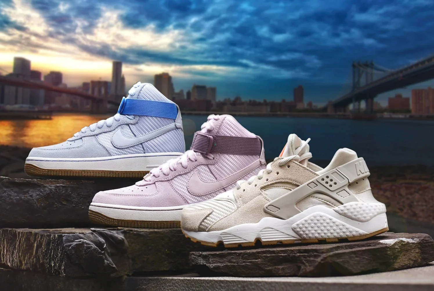 Three pairs of sneakers styled on rocks along the NYC waterfront, with the Brooklyn Bridge and skyline at sunset in the background — commercial product and lifestyle photography.