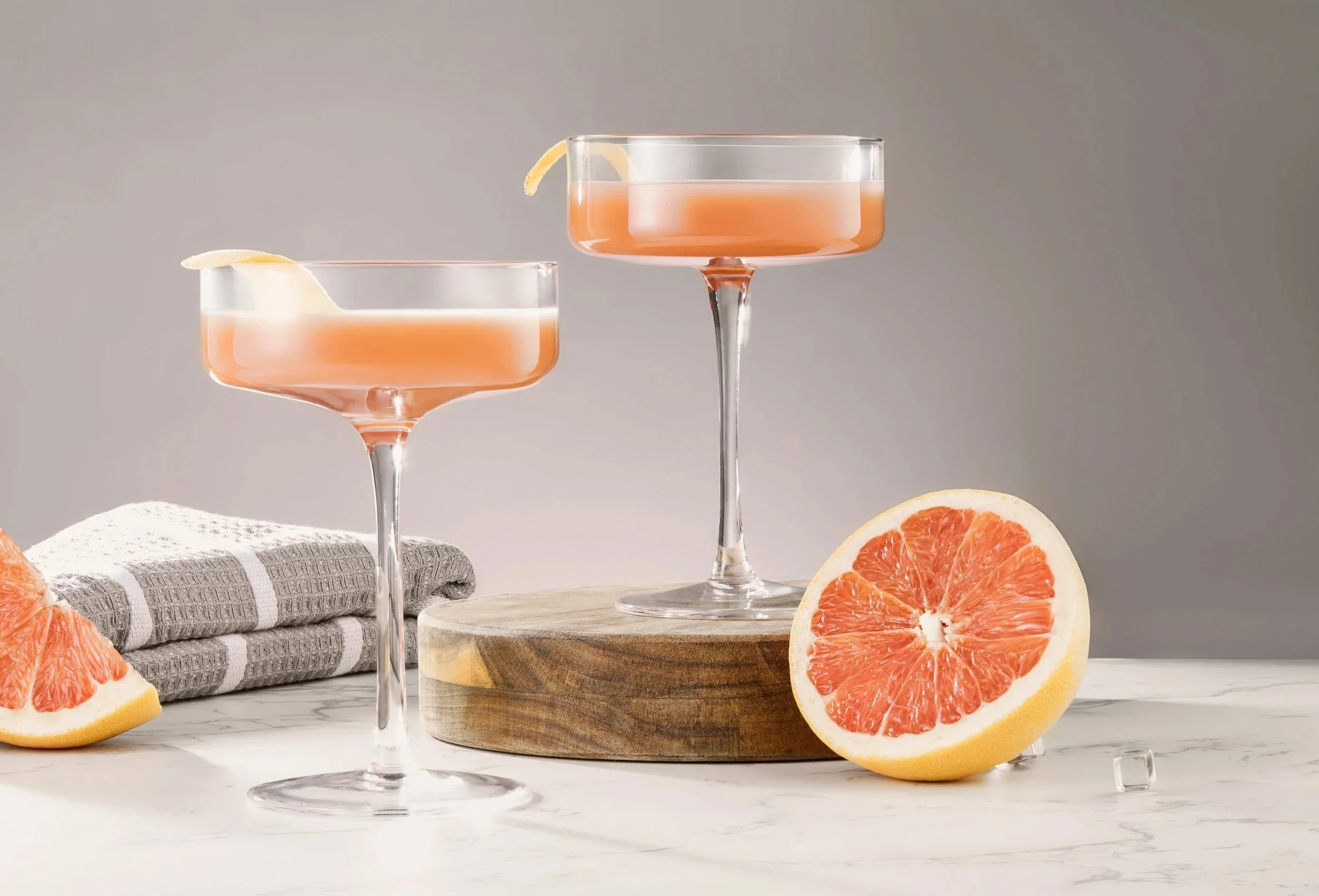 Two coupe glasses of pink drinks styled with grapefruit.