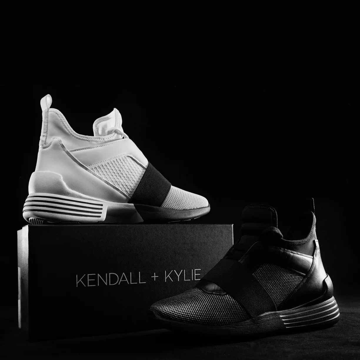Black and white campaign shot of two Kendall + Kylie sneakers displayed on their branded box, dramatic lighting — commercial footwear and brand photography.