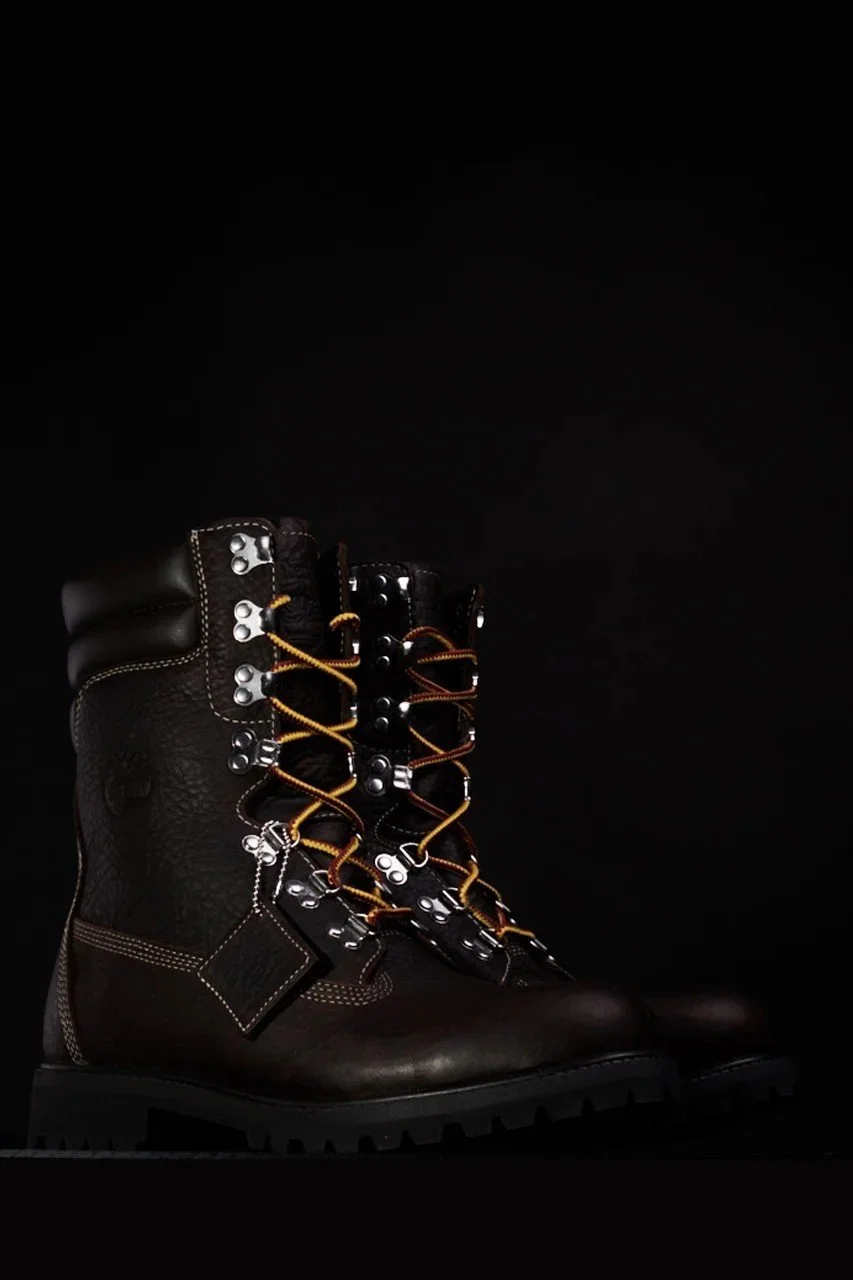 Dark brown leather boots with contrast laces, metal eyelets, and thick rubber soles, styled against a black background — commercial product photography.