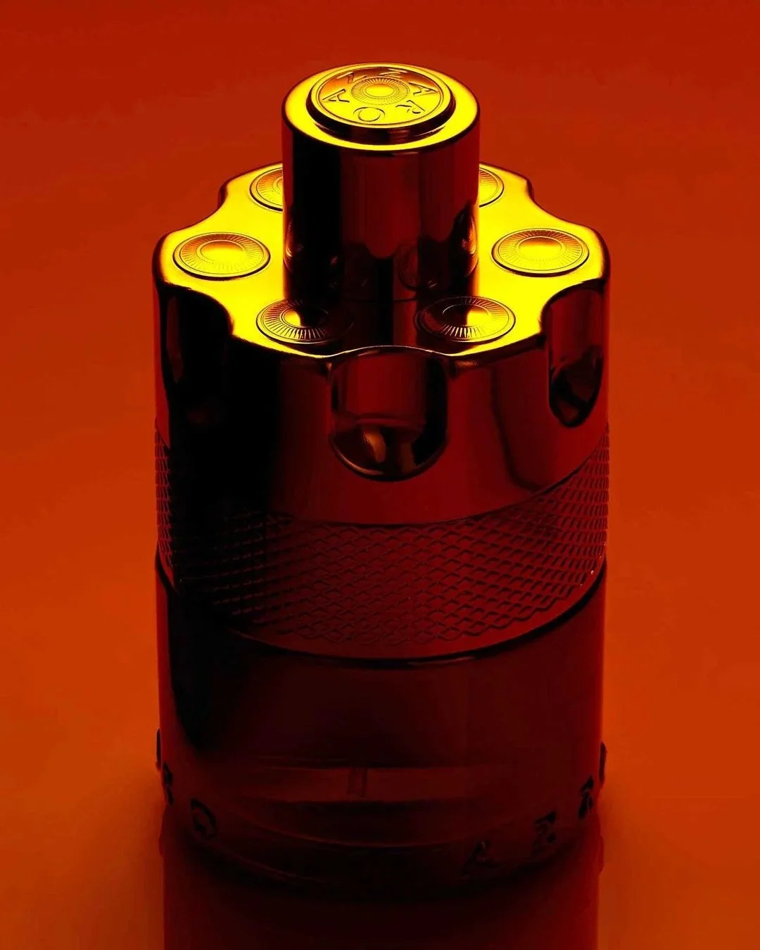 Fragrance bottle illuminated in red and gold against an orange background.