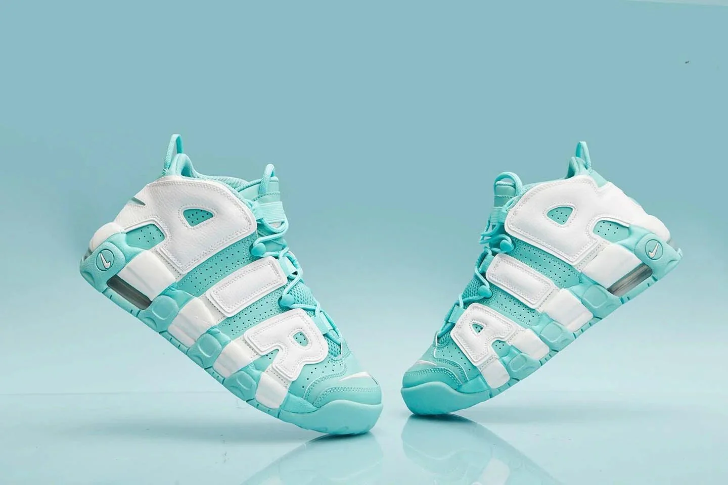 Pair of white and turquoise Nike Air More Uptempo sneakers photographed against a matching turquoise background — color-blocked commercial product photography.