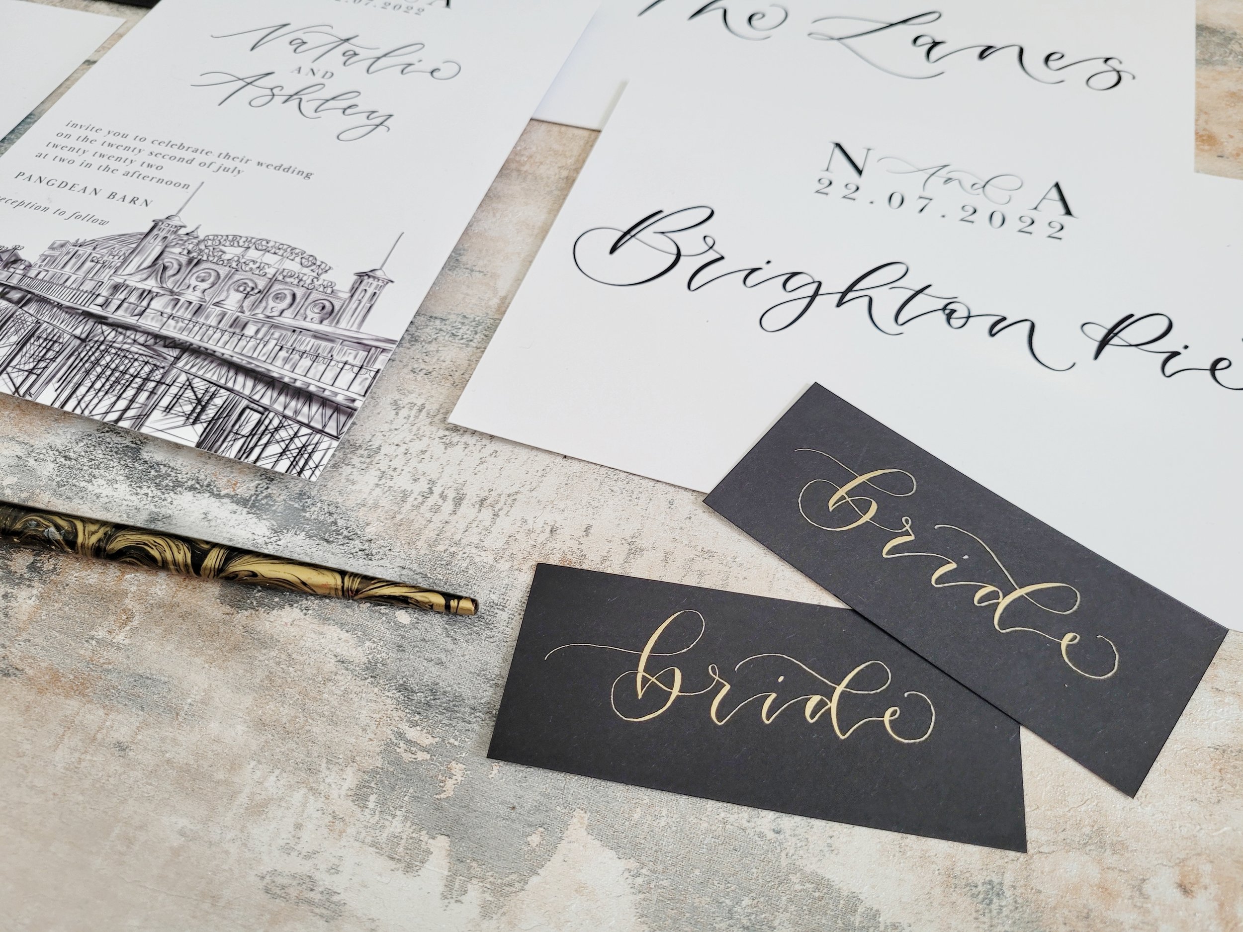 Brighton wedding stationery with pier illustration and modern calligraphy - monochrome minimalist invitation set - with black and gold place cards and Brighton themed table numbers.jpeg